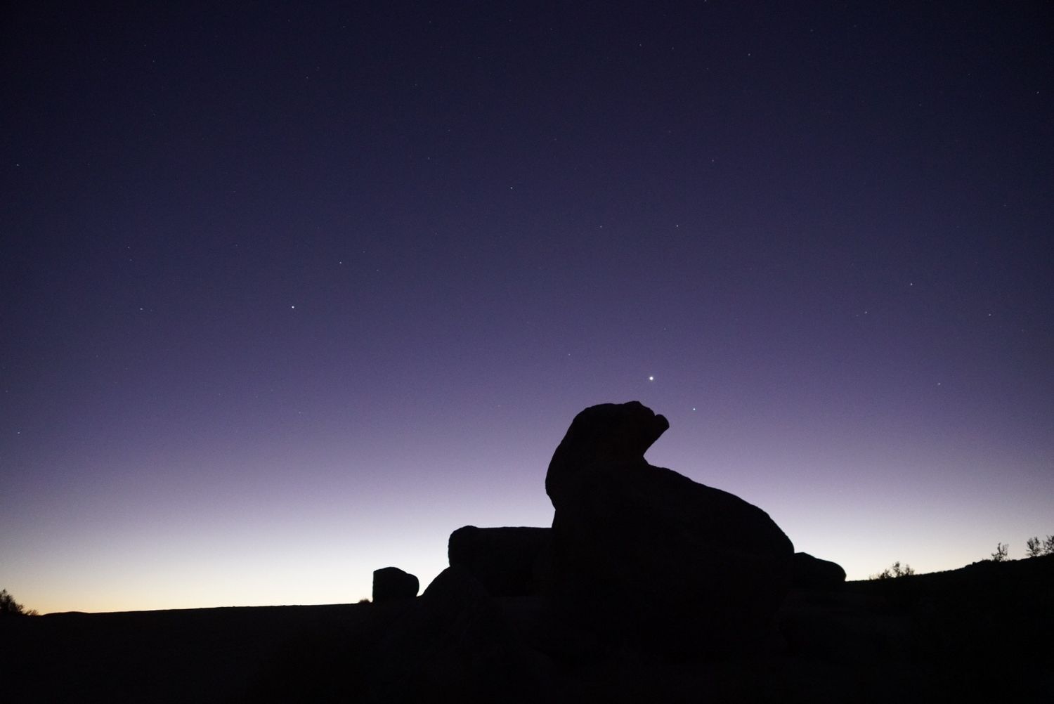 Large rock formation silhouetted against purple starry night sky at dusk.