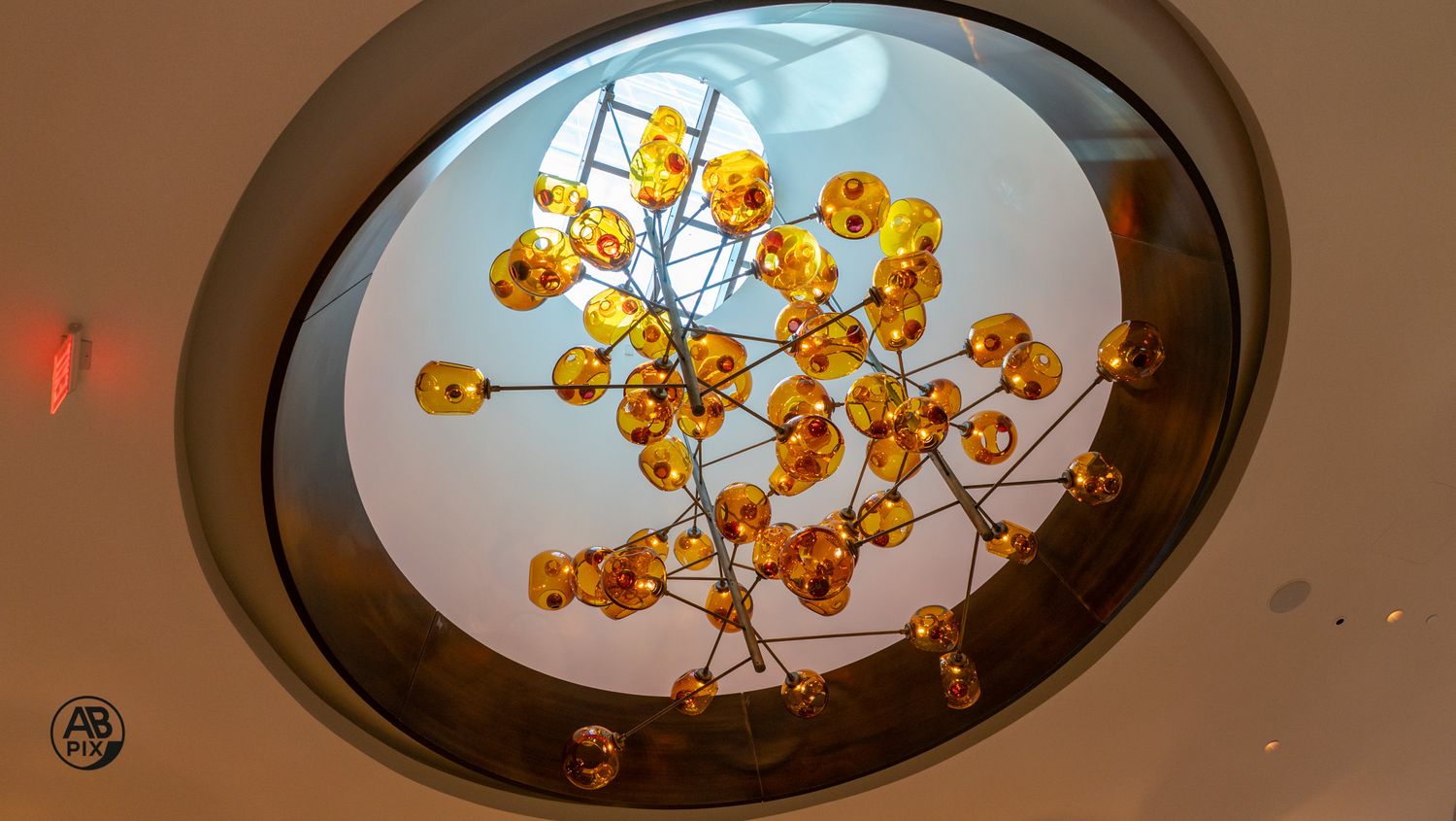 Artistic amber glass sphere chandelier viewed from below within circular ceiling skylight.