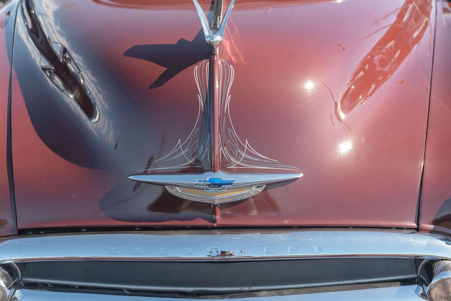 Close-up of a vintage red car hood ornament with a sleek chrome bird design on a polished burgundy surface.