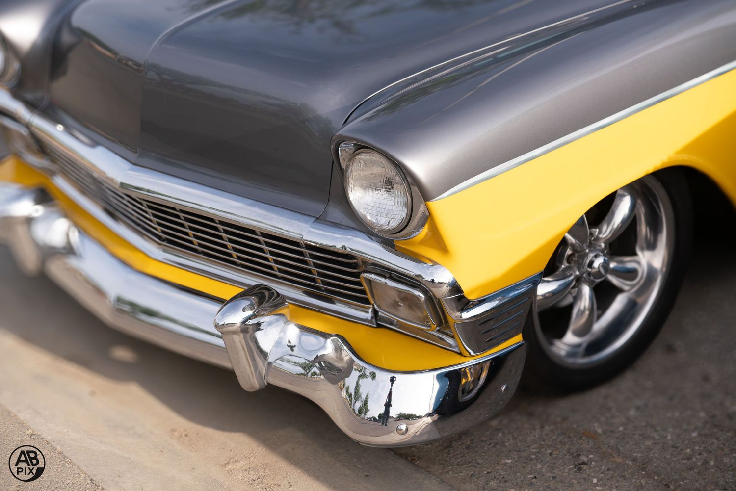 Front detail of a two-tone gray and yellow custom 1956 Chevrolet with chrome bumper and alloy wheels.