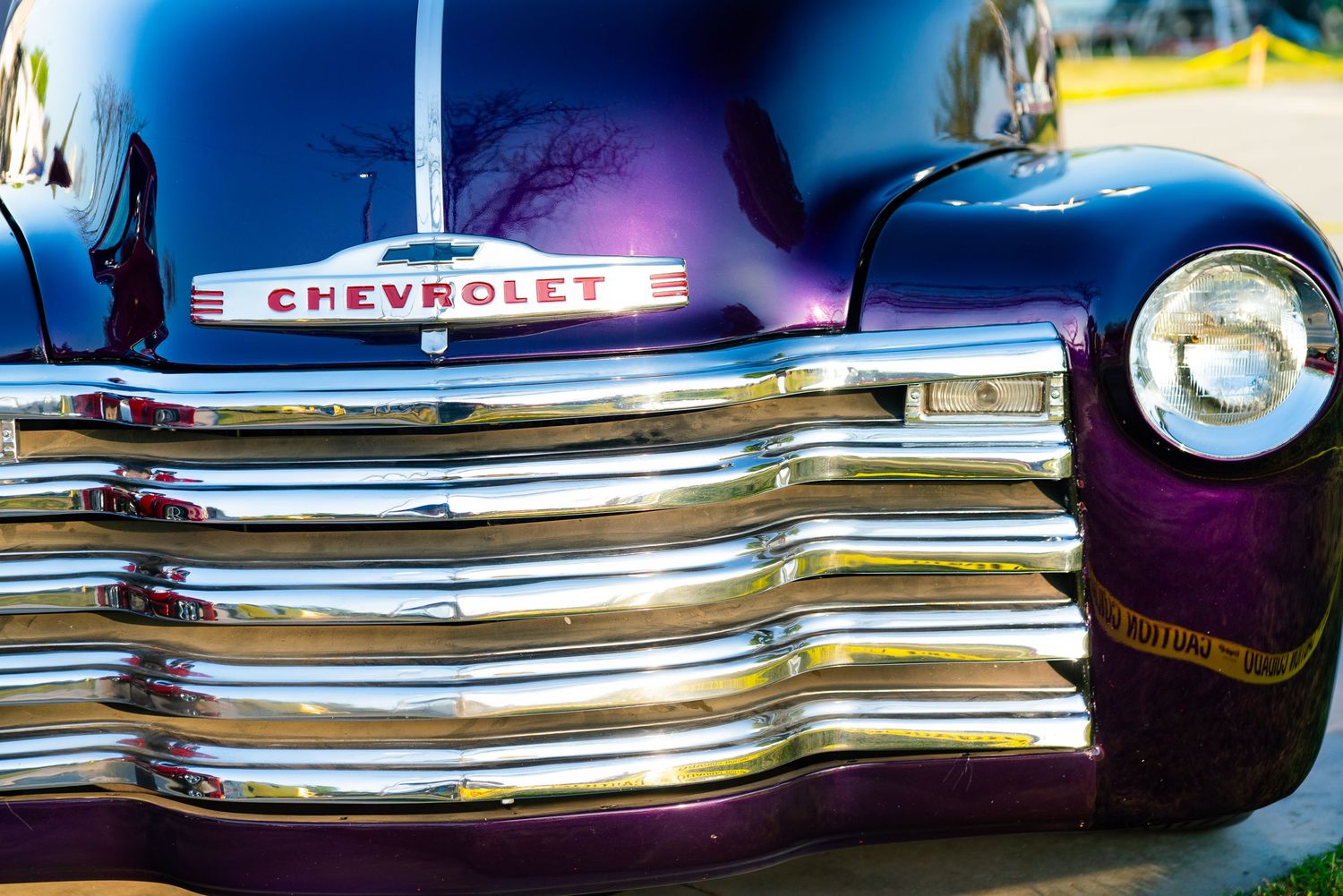 Close-up of a vintage purple Chevrolet truck featuring a polished chrome grille and headlight.