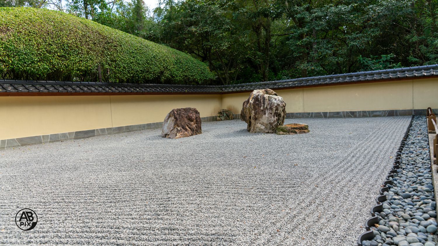 Serene Japanese zen rock garden with raked gravel and natural stone boulders beside a clay wall.