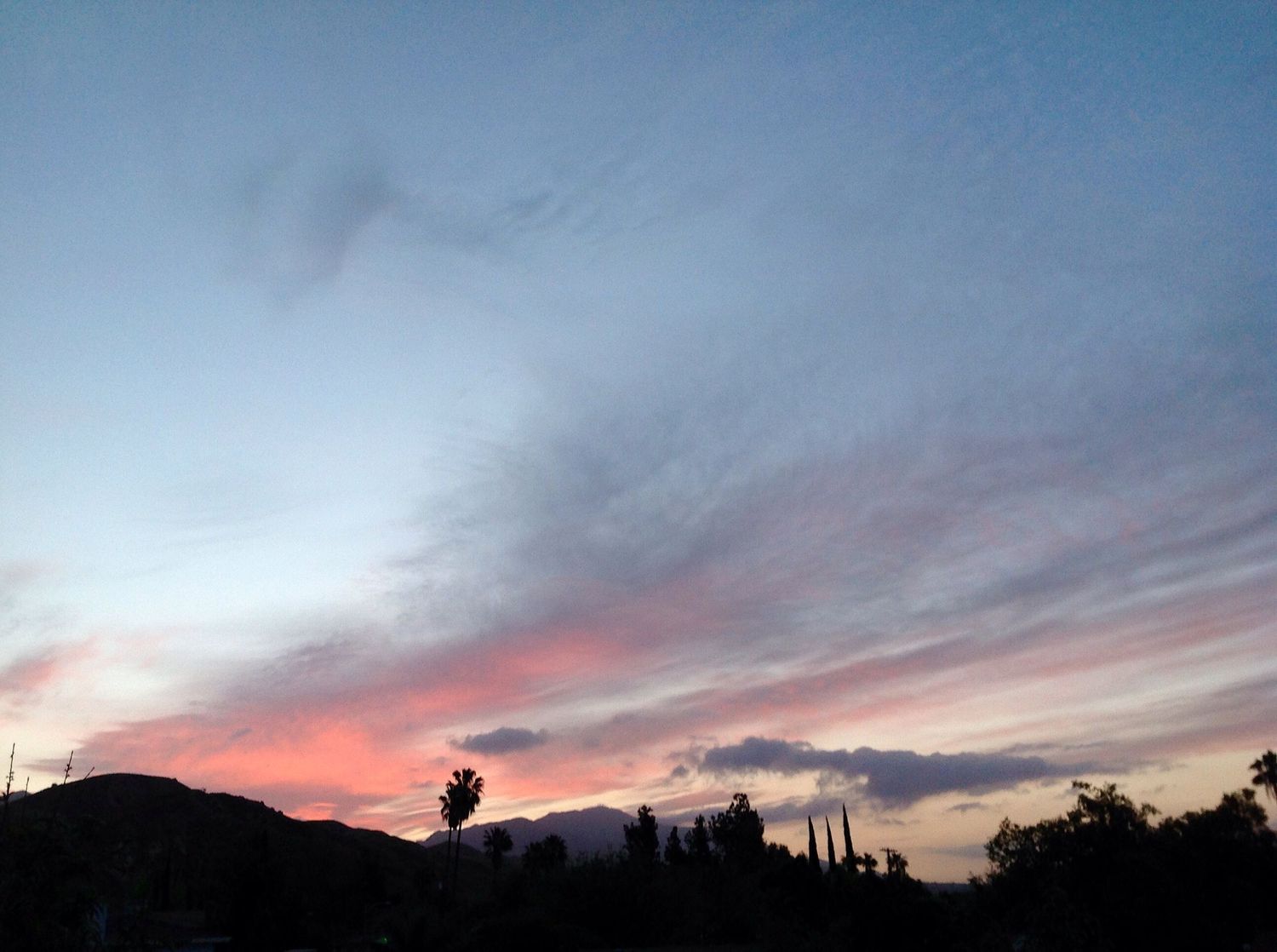 Soft pastel blue and pink sunset sky with wispy clouds over silhouetted hills and trees.