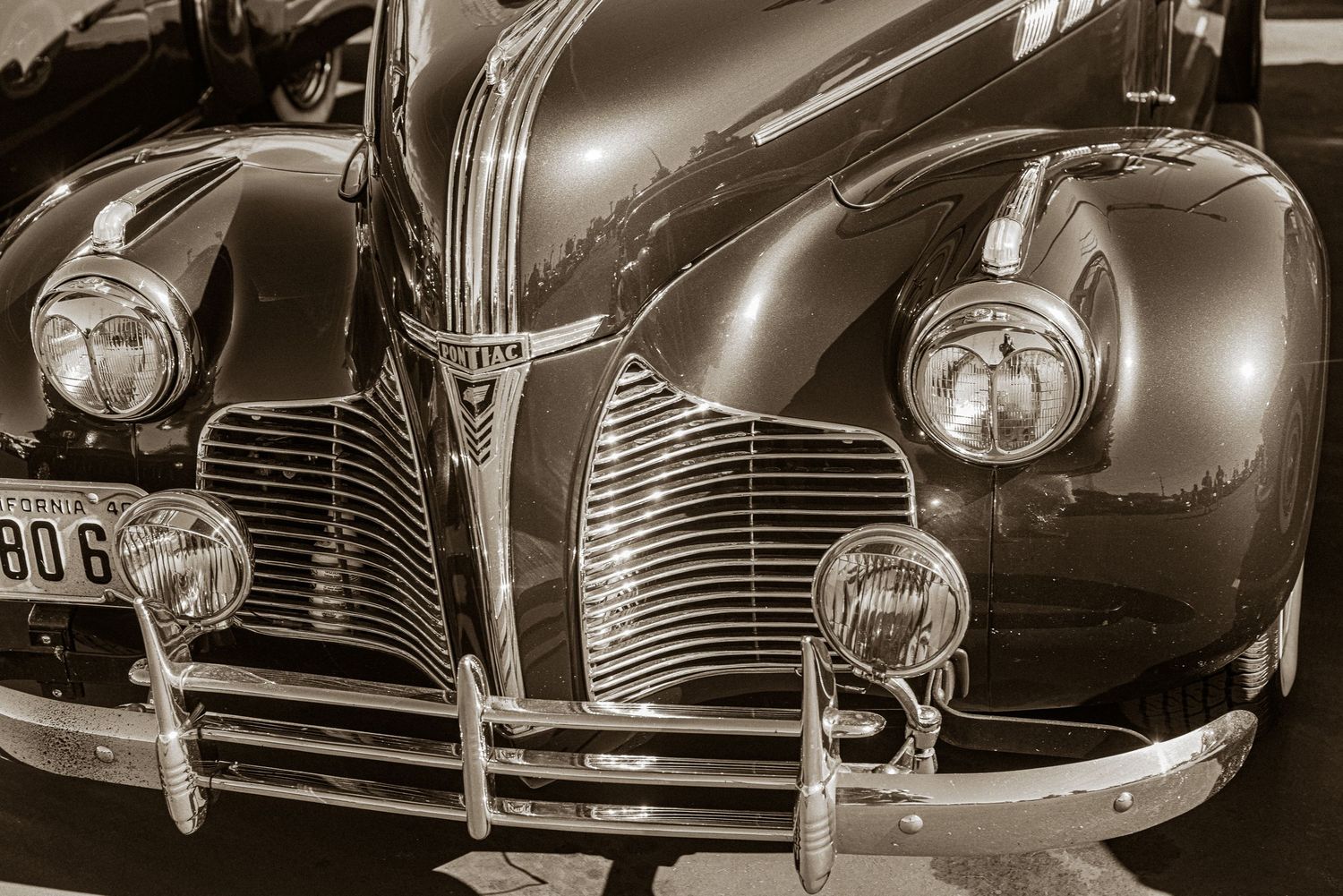 Sepia-toned close-up of a vintage classic car front grille with round headlights and chrome details.