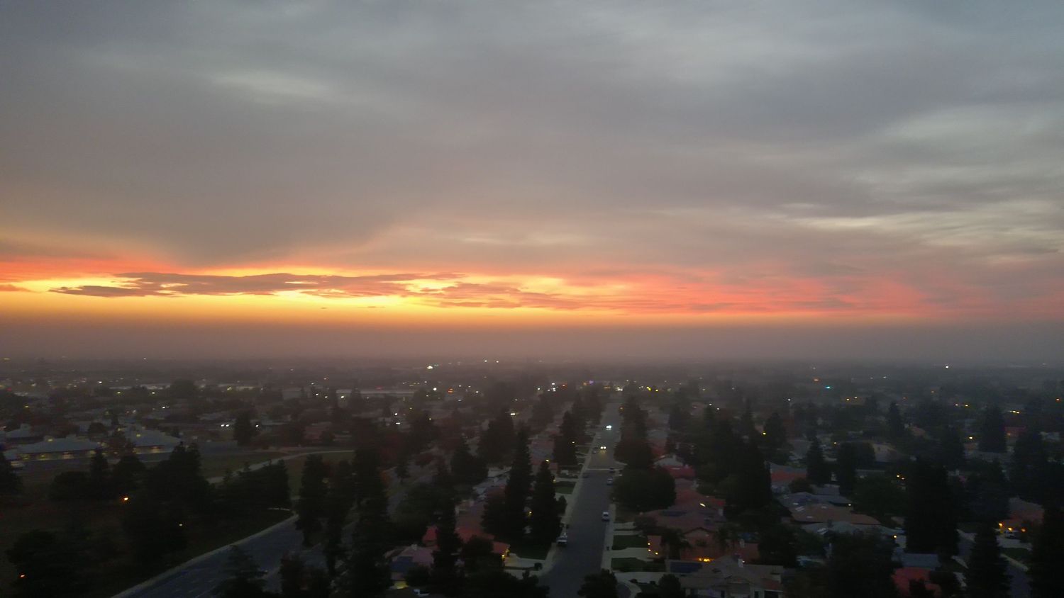 Aerial view of suburban cityscape at sunset with colorful orange and pink sky.