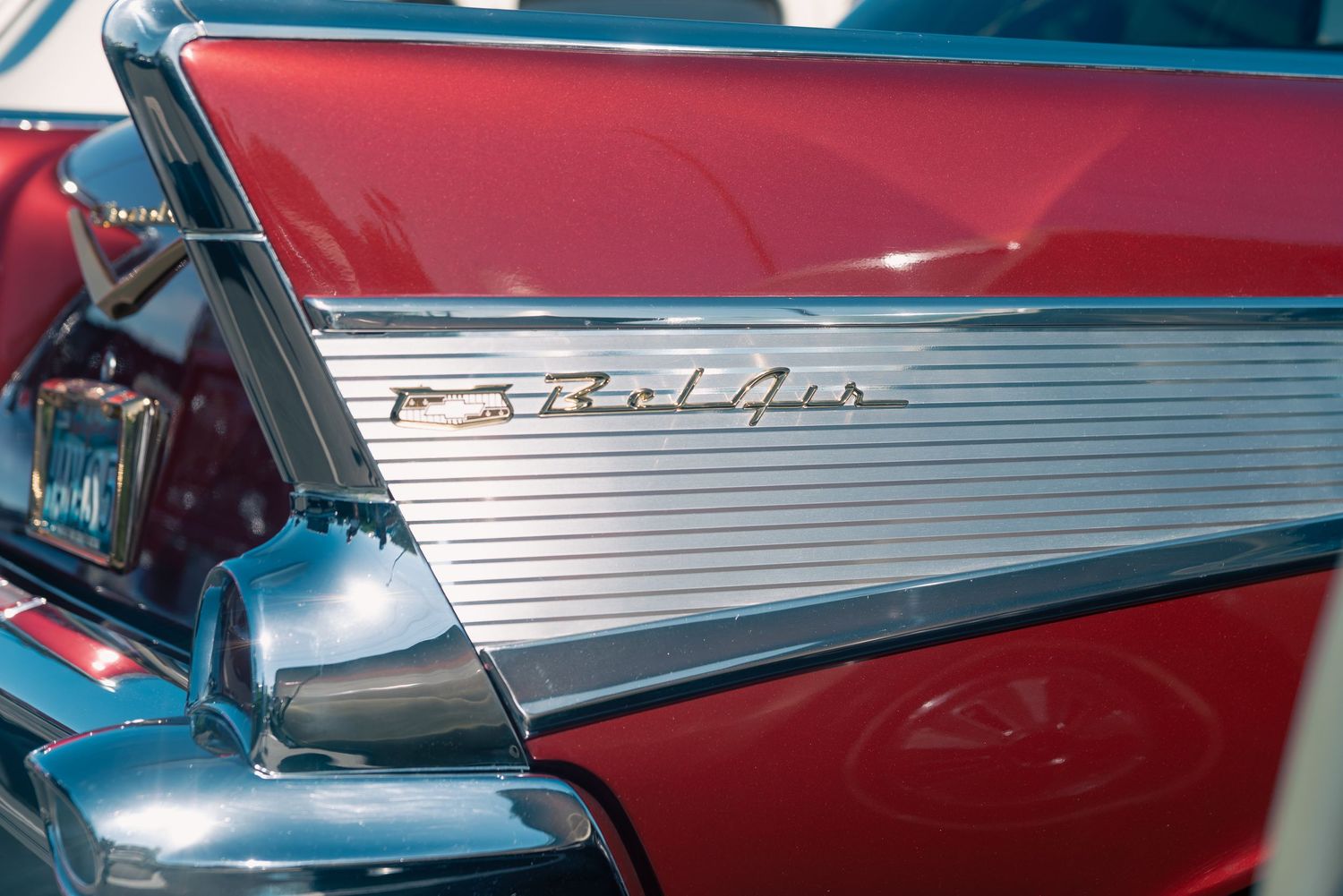 Close-up of a classic red Chevrolet Bel Air chrome tail fin badge at a vintage car show.