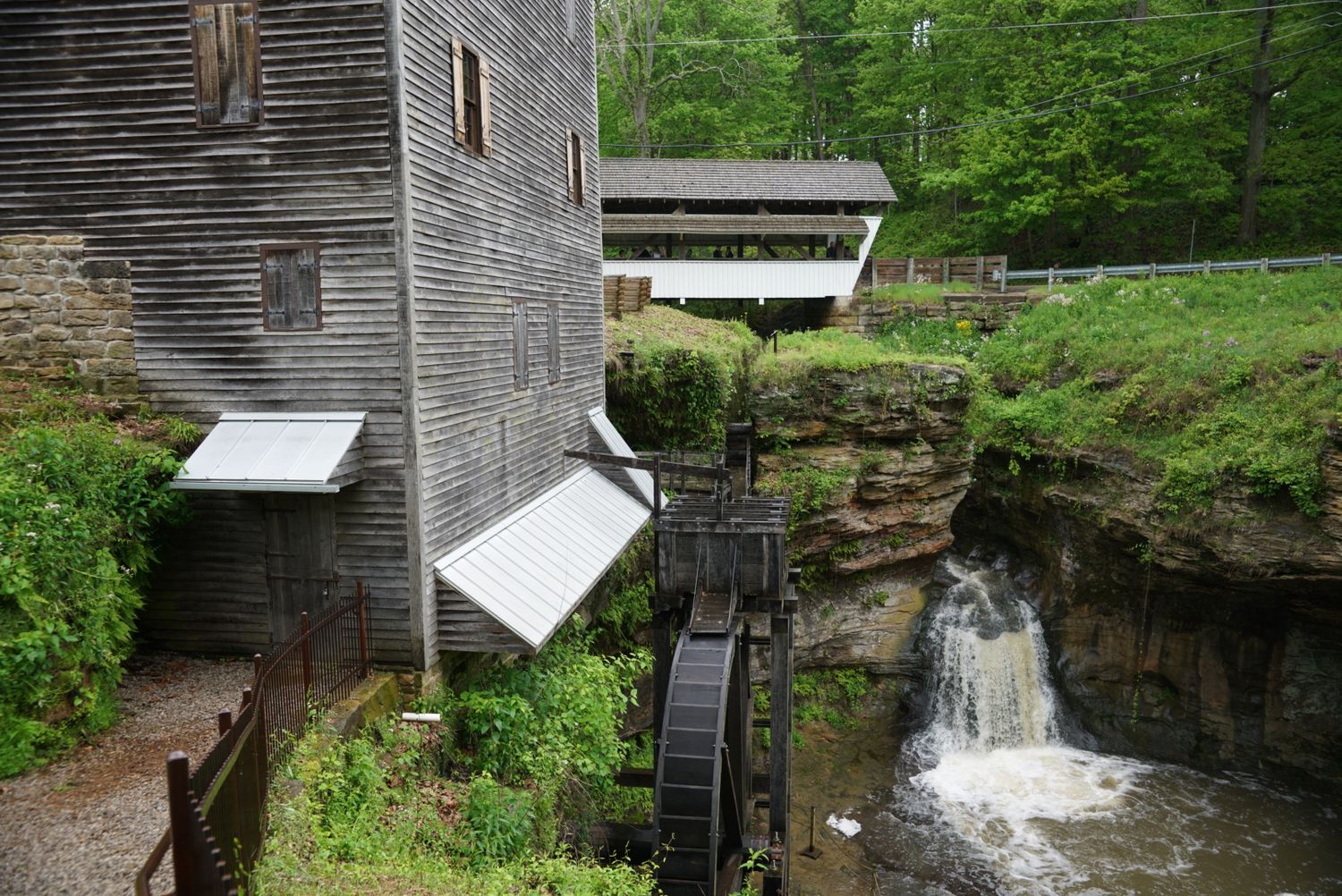 Historic grist mill with wooden waterwheel beside a rocky waterfall in a lush wooded ravine.