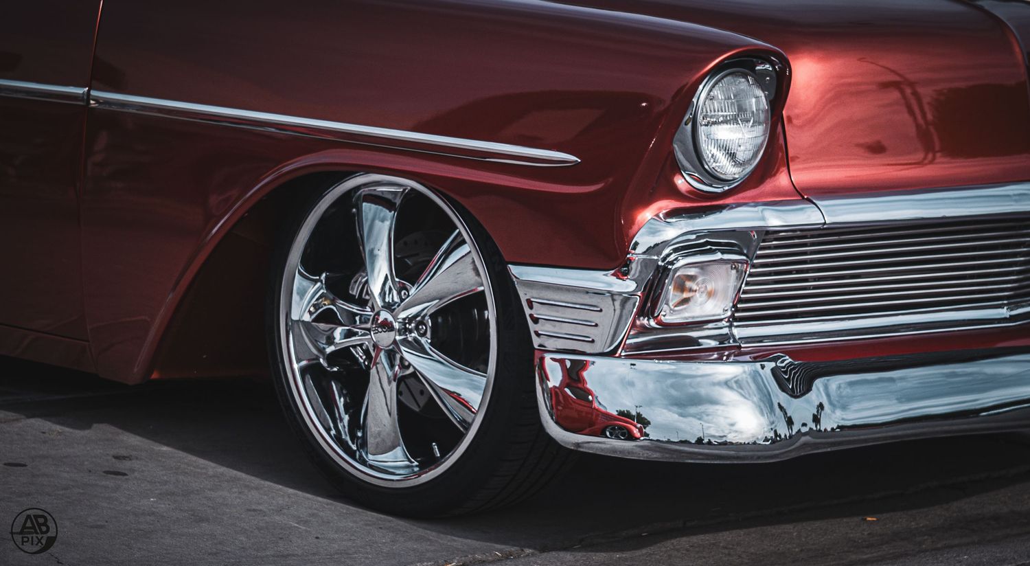 Candy red 1956 Chevrolet Bel Air with chrome bumper and custom wheels, low angle.