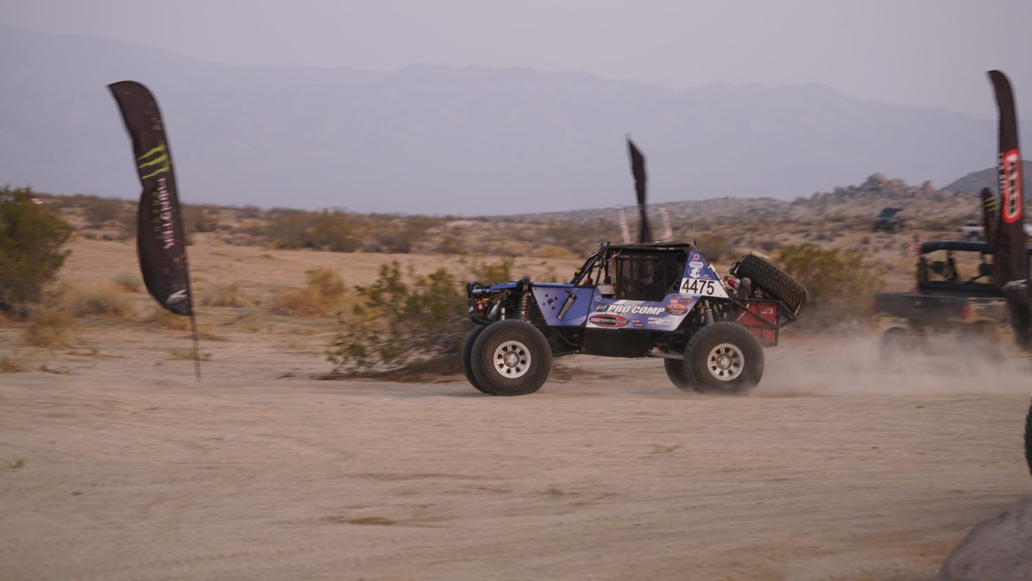 Off-road buggy racing through desert terrain kicking up dust near Monster Energy banners.