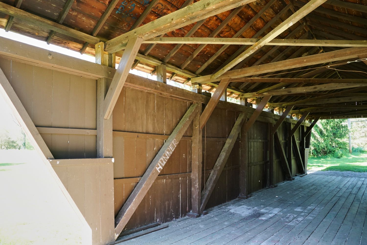 Interior of a rustic wooden covered bridge showing aged timber beams, diagonal bracing, and weathered plank flooring.