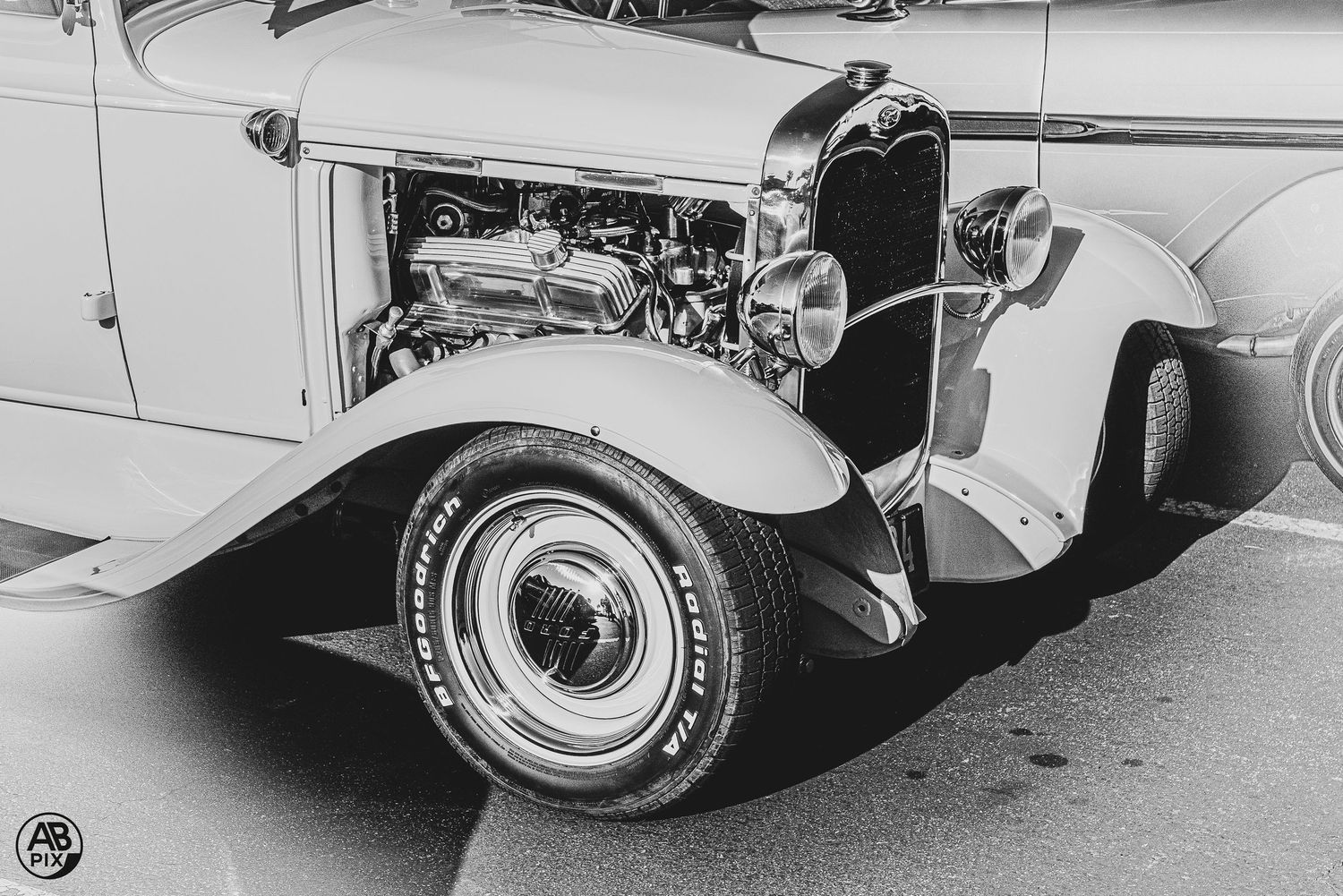 Black and white photo of a vintage hot rod with exposed engine, whitewall tires, and open hood.