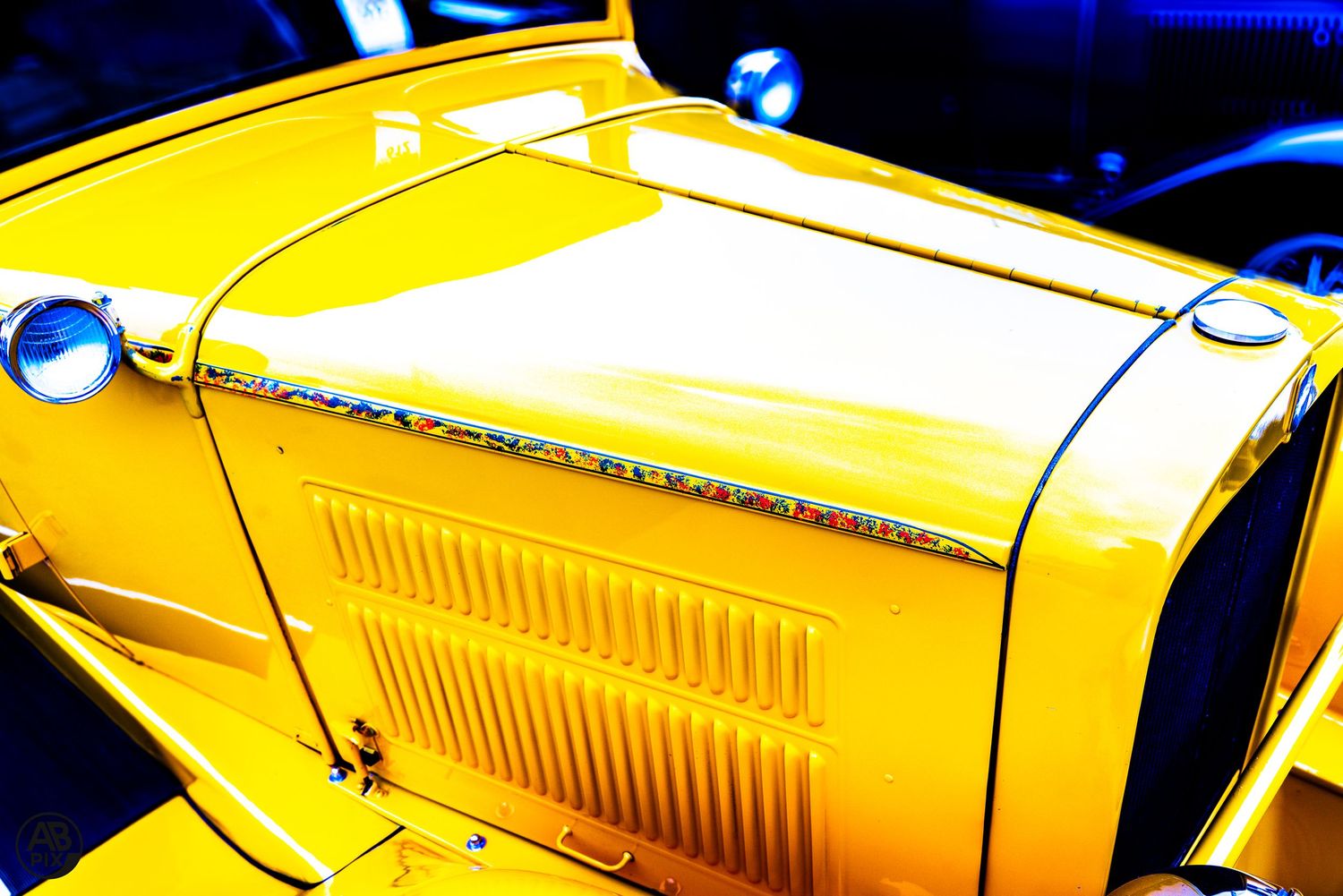 Vibrant yellow vintage hot rod car hood with chrome details and blue accent lighting.