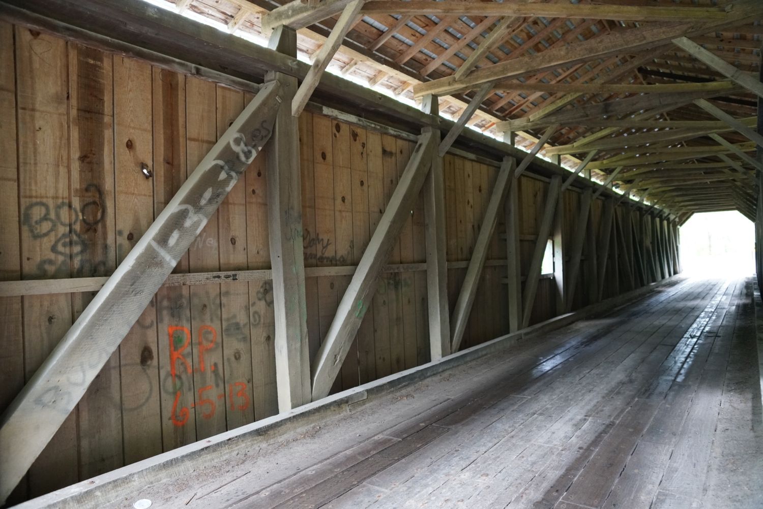 Interior of a historic wooden covered bridge showing timber truss construction and graffiti.