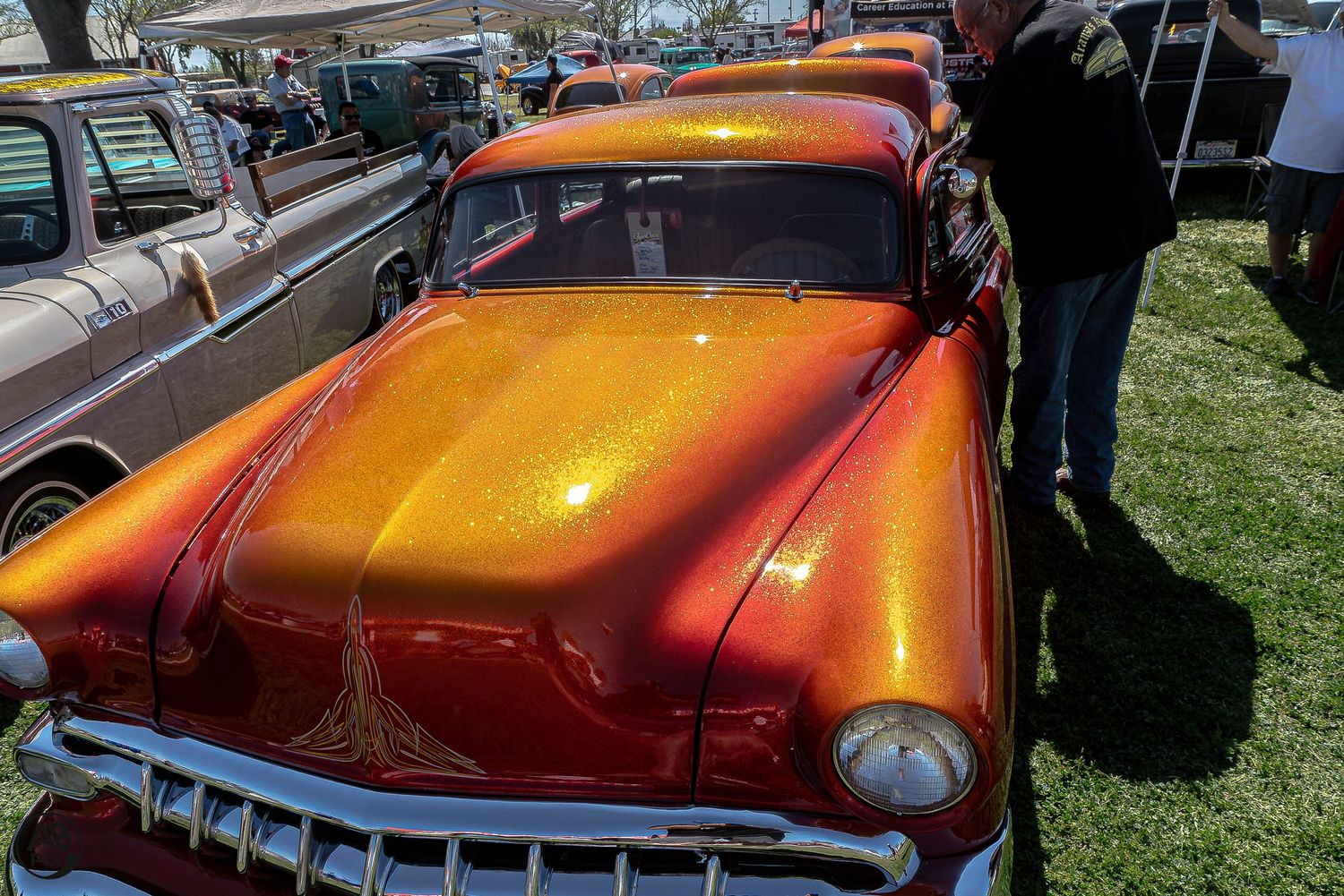Shiny orange metallic flake custom classic car at an outdoor car show.