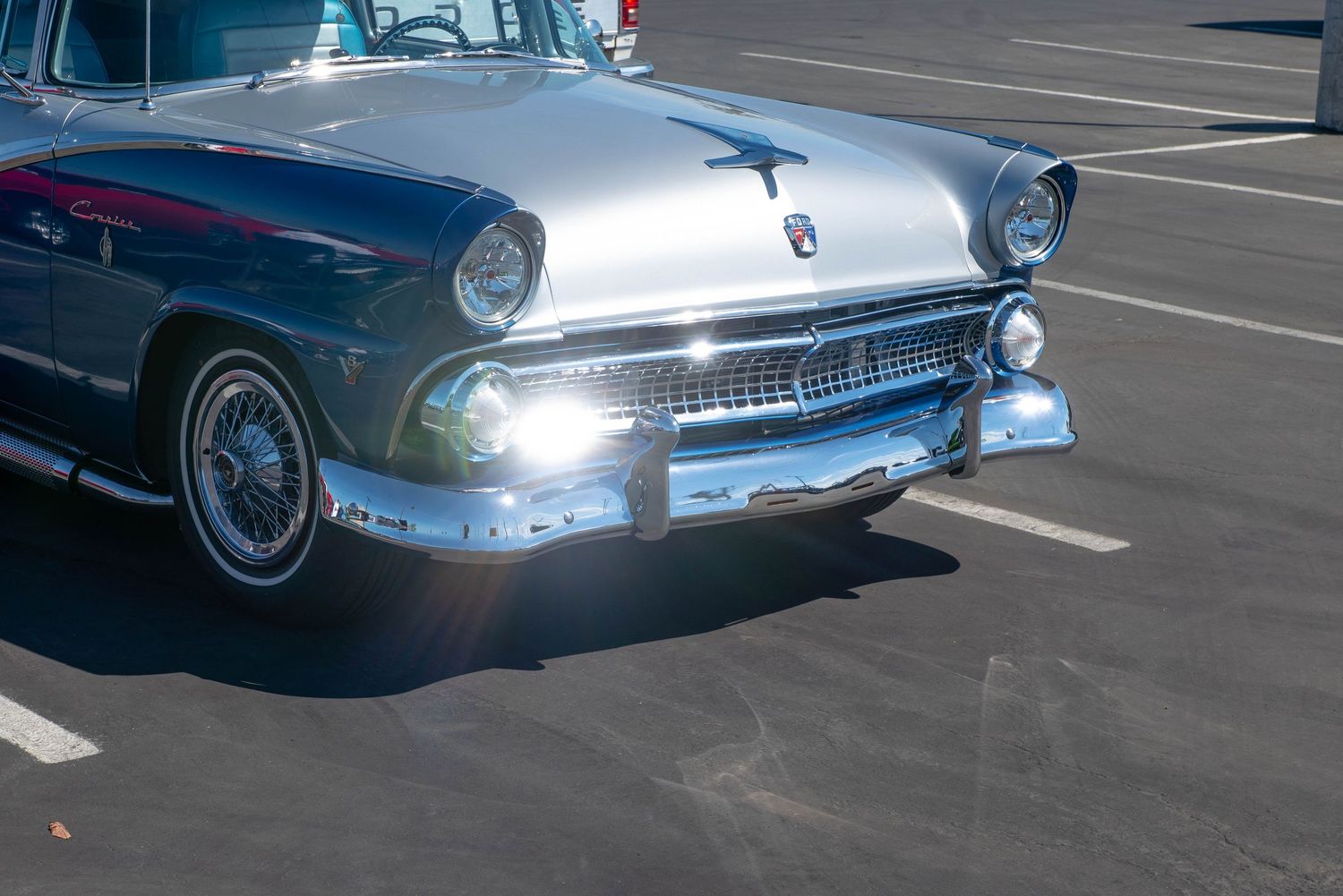Close-up front view of a restored 1955 Ford Crown Victoria with shining headlights and chrome bumper detail.