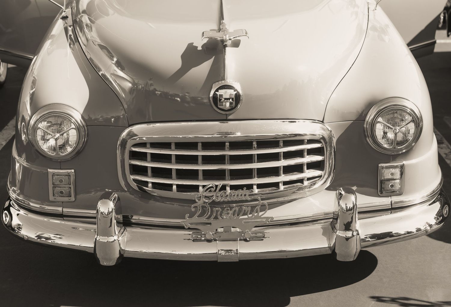 Vintage black and white photo of a classic car front grille and headlights at a car show.