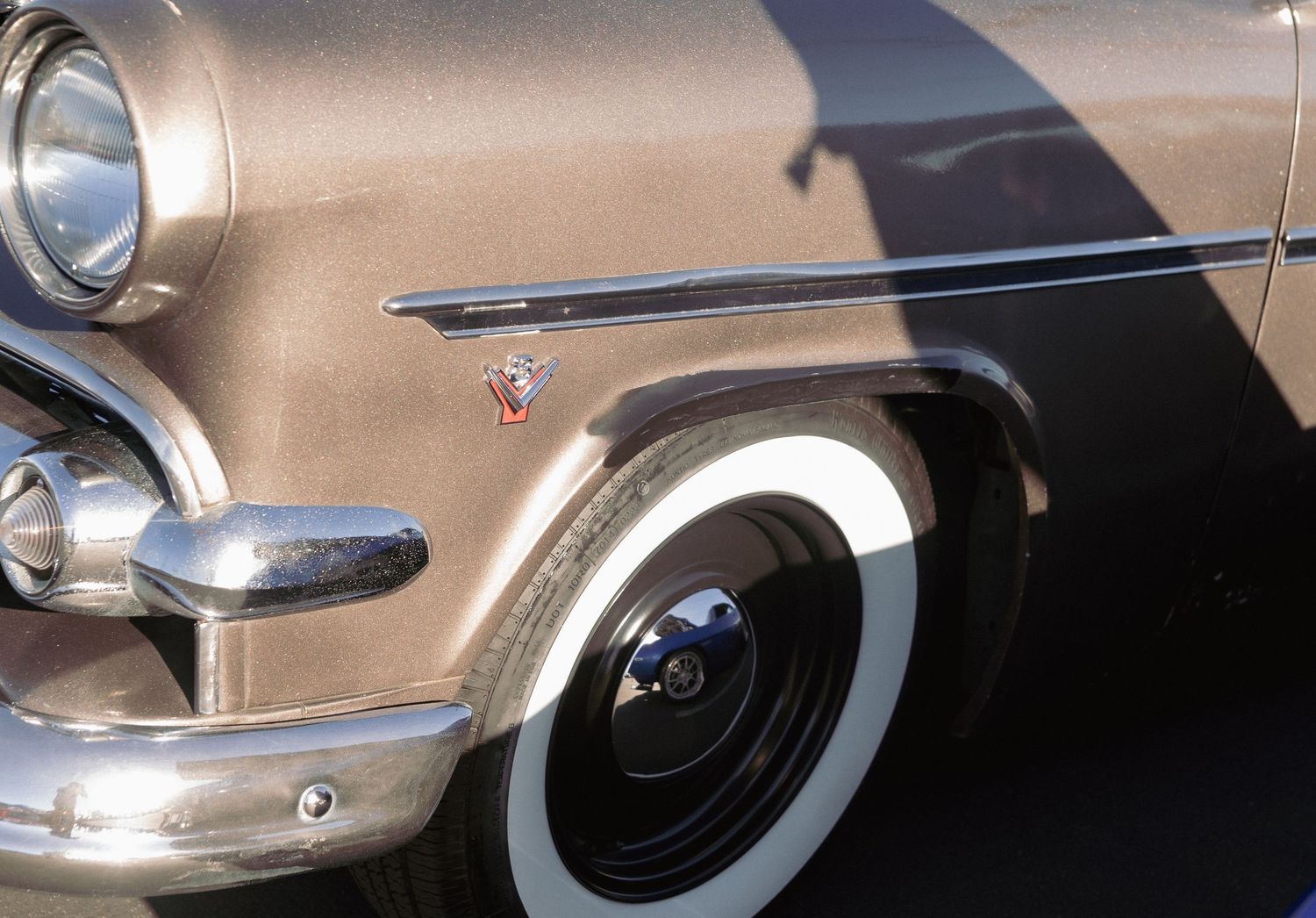 Close-up of a vintage classic car featuring a white sidewall tire and chrome details on a tan body.
