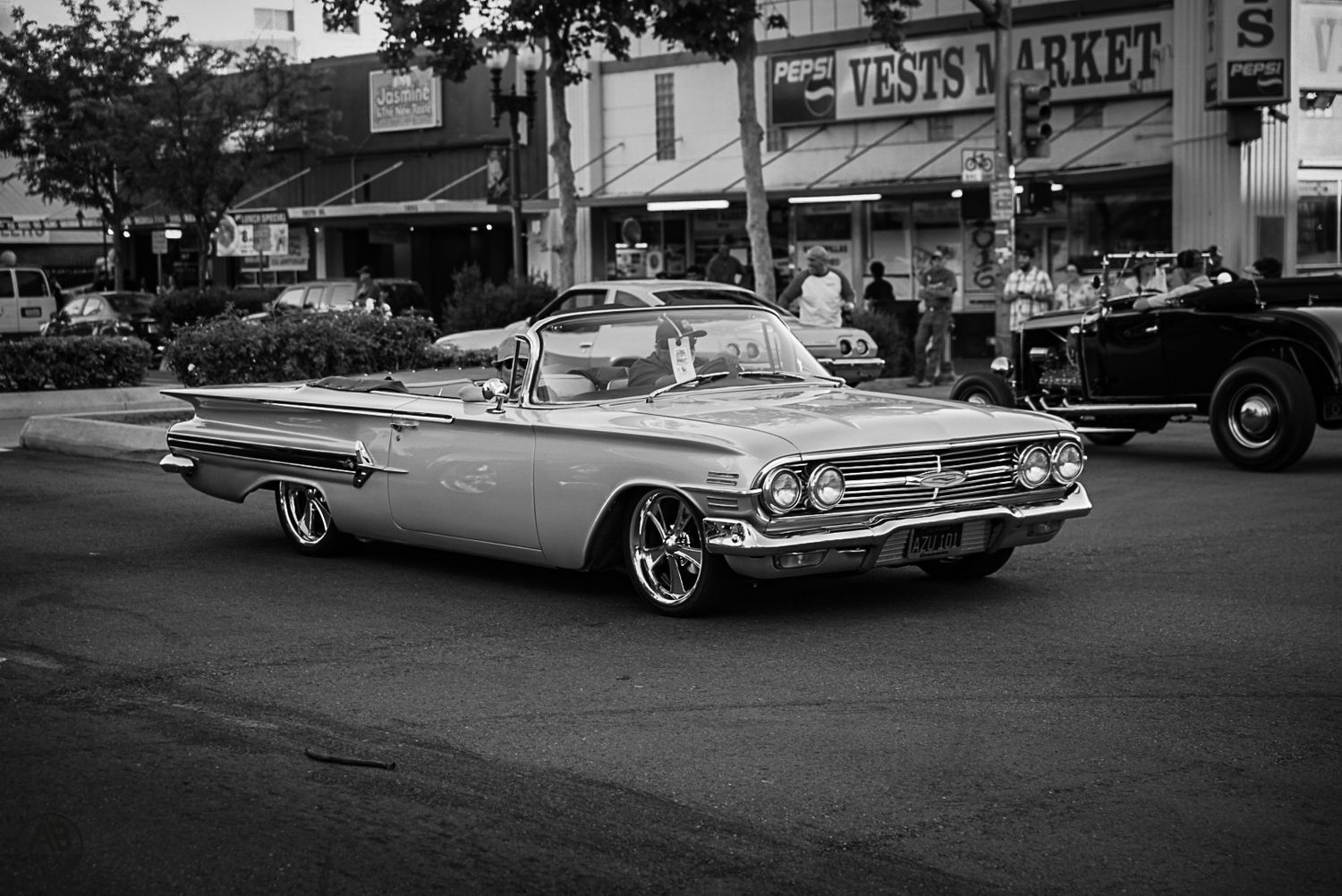 Black and white photo of a classic 1960 Chevrolet Impala cruising down a street.