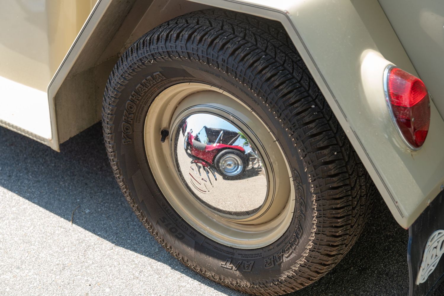 Close-up of a tan vintage vehicle tire with chrome hubcap reflecting a red classic car.