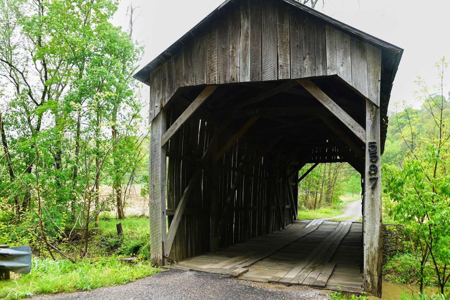 Rustic wooden covered bridge surrounded by lush green trees on a quiet country road.