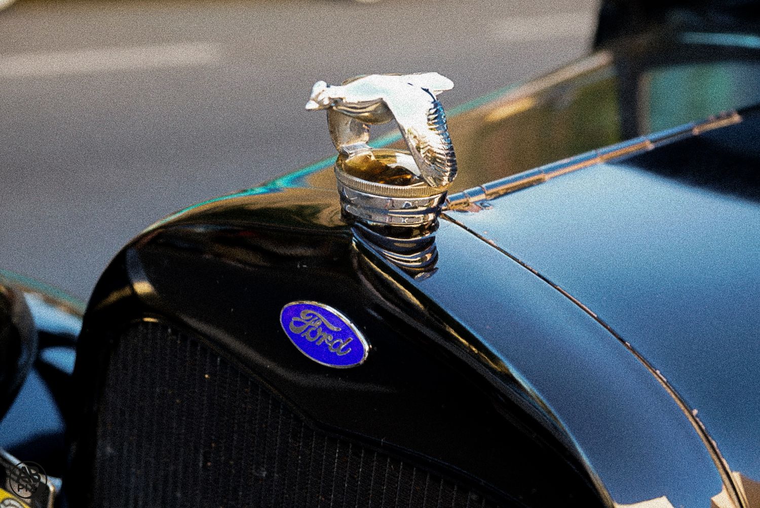Vintage Ford classic car hood ornament and blue oval emblem on a shiny black vehicle.