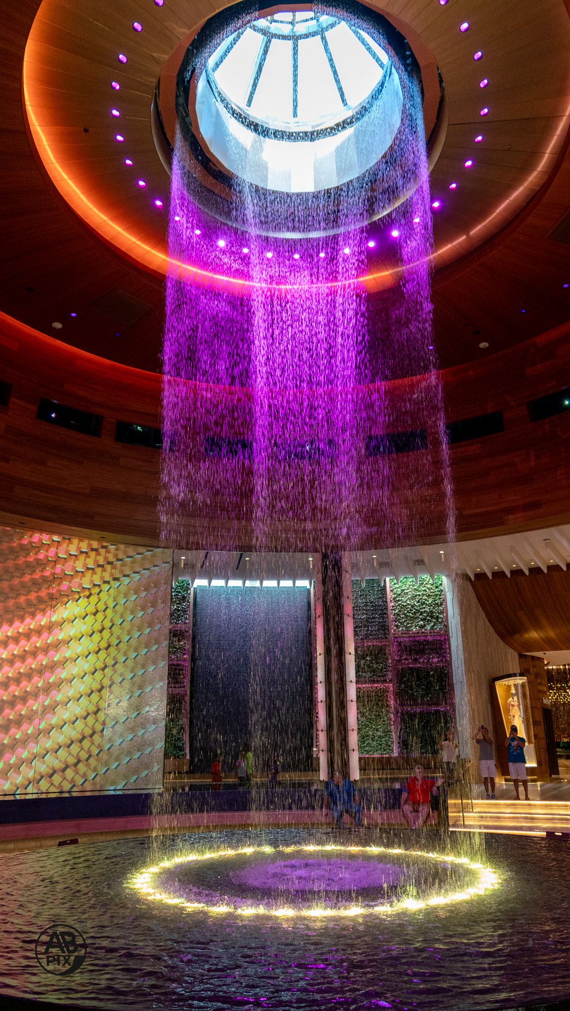 Stunning indoor waterfall with purple LED lights under circular skylight in luxury venue.
