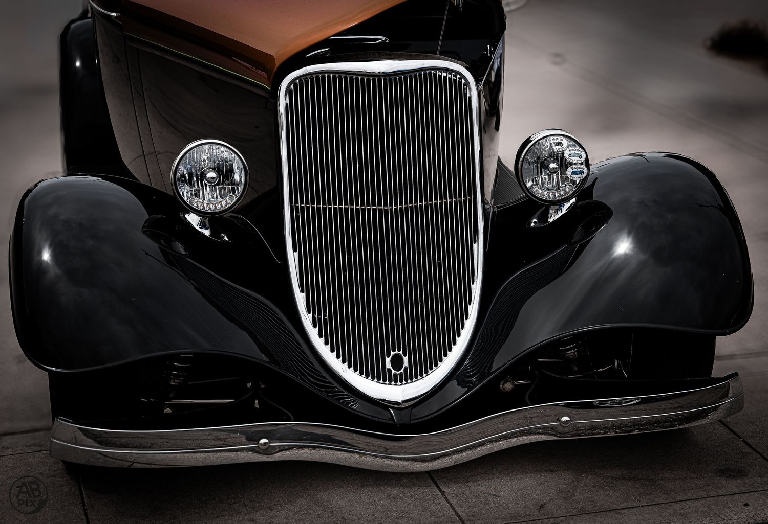 Front view of a sleek black 1930s classic car with chrome grille and round headlights.