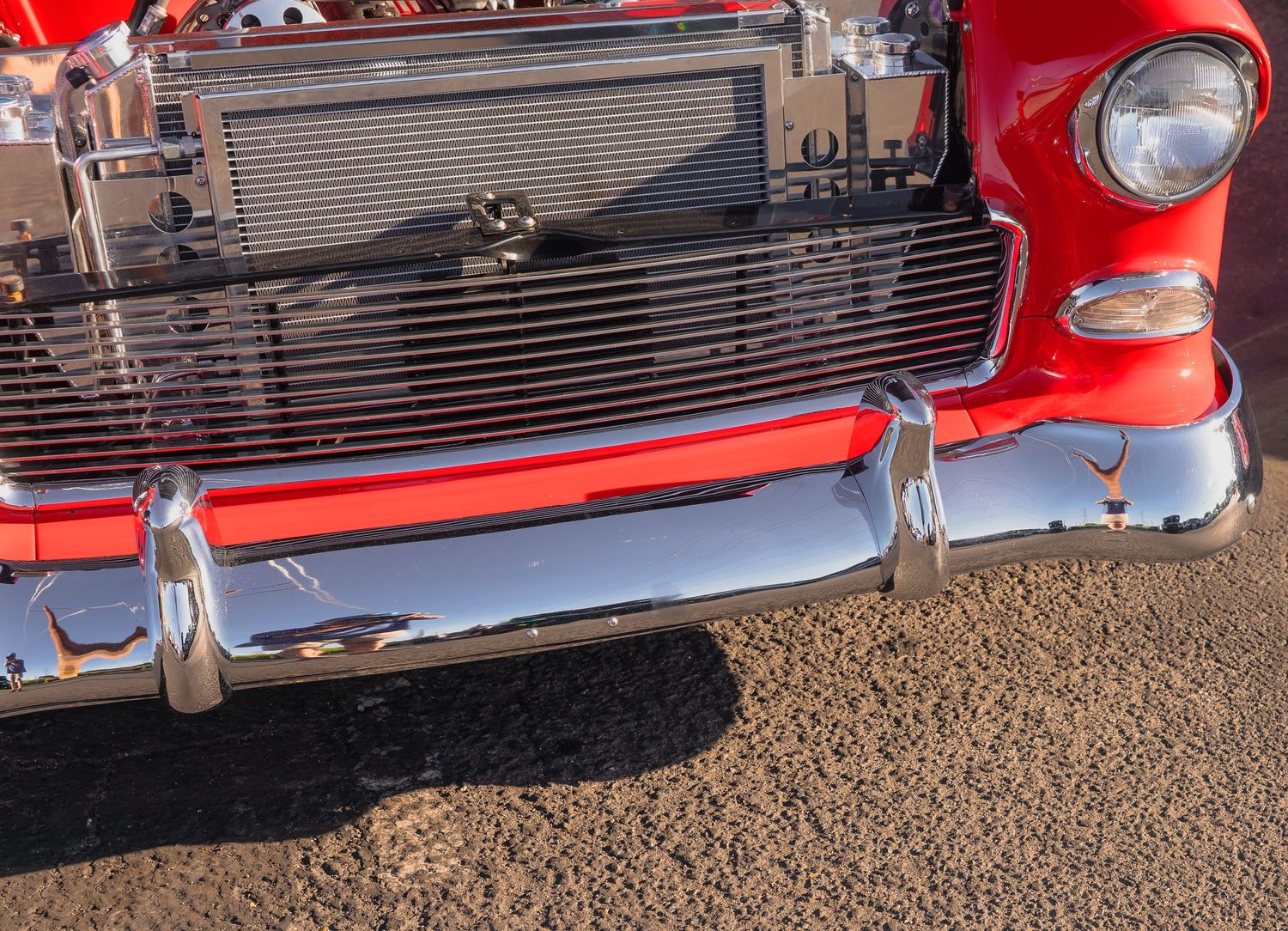 Close-up of a classic red 1955 Chevy Bel Air chrome front bumper and grille at a car show.