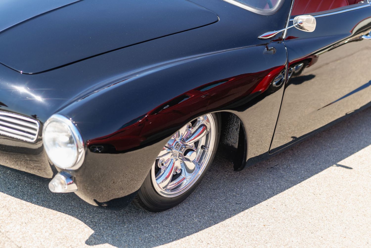 Close-up of a classic custom black car with chrome wheels and red interior, showcasing vintage automotive design.