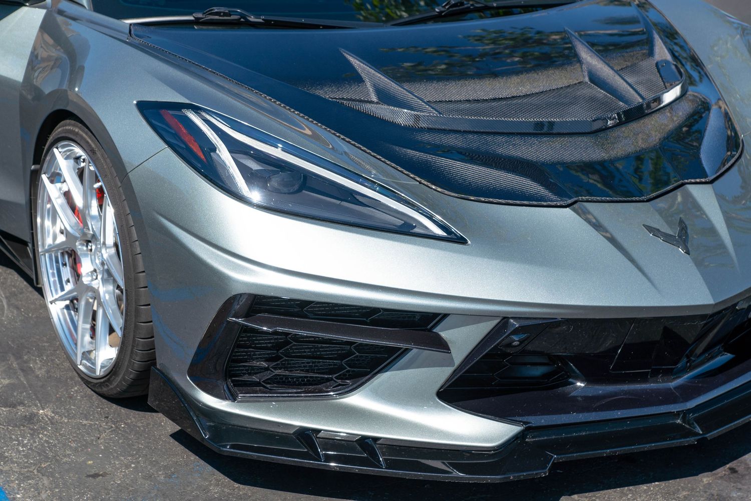 Front corner view of a modern silver C8 Chevrolet Corvette with chrome wheels and carbon fiber hood details.