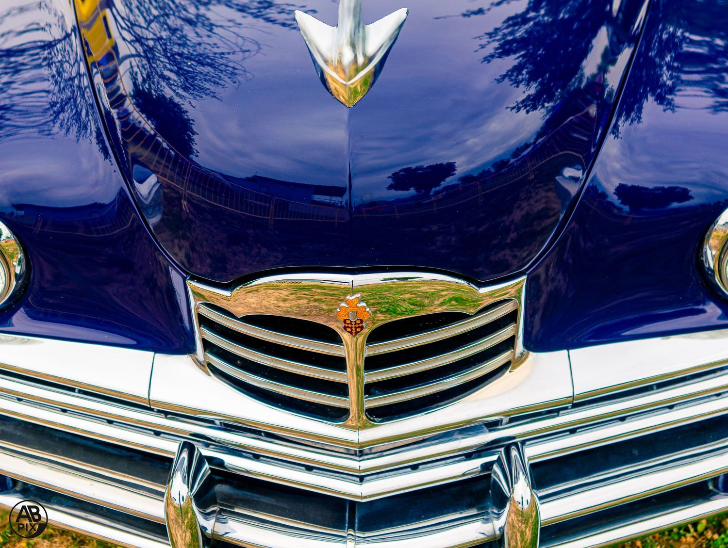 Deep blue classic car front grille and hood ornament with chrome detailing at vintage auto show.