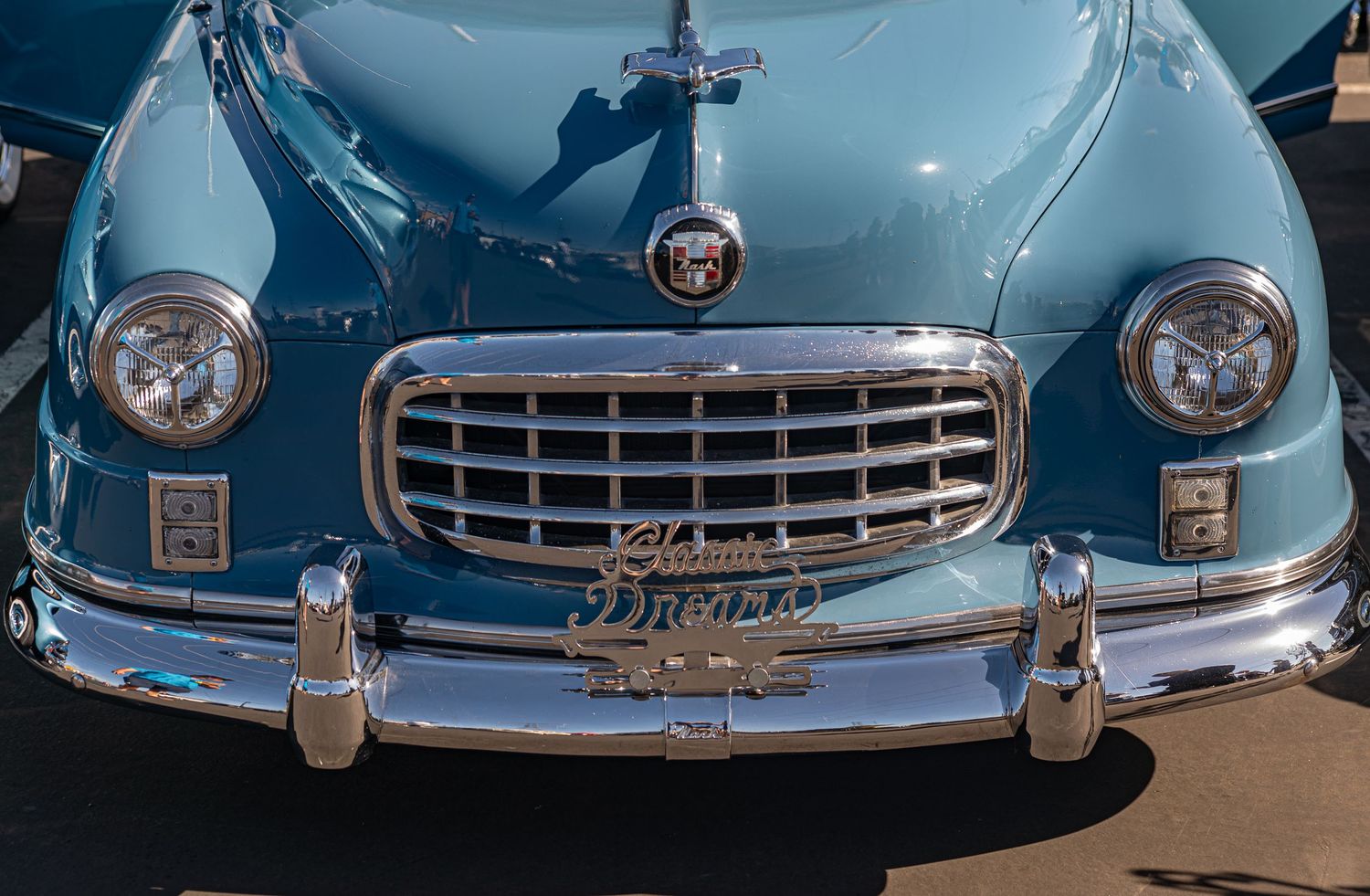 Vintage light blue classic car front view showing chrome grille and headlights at an outdoor car show.