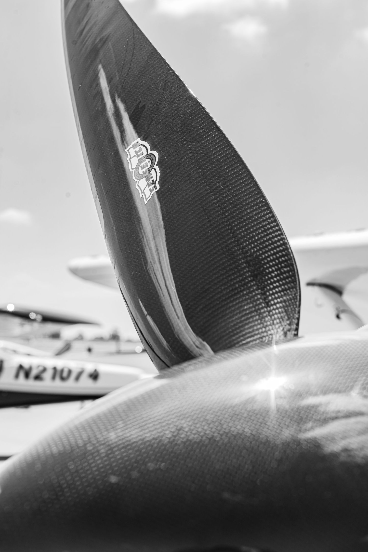 Close-up black and white photo of a carbon fiber aircraft propeller blade at an airshow.