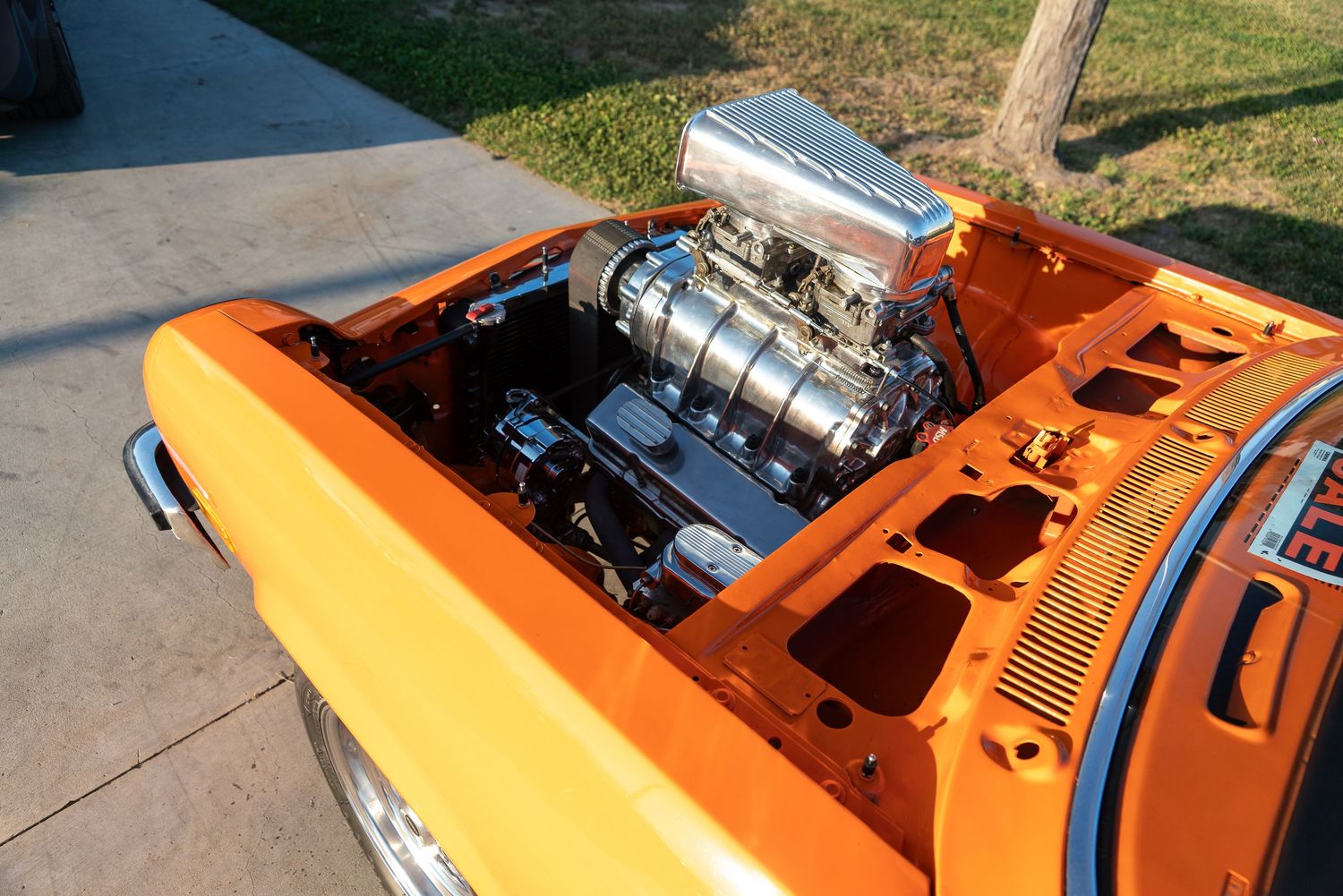 Orange classic car with polished supercharged V8 engine on display, hood open at outdoor car show.