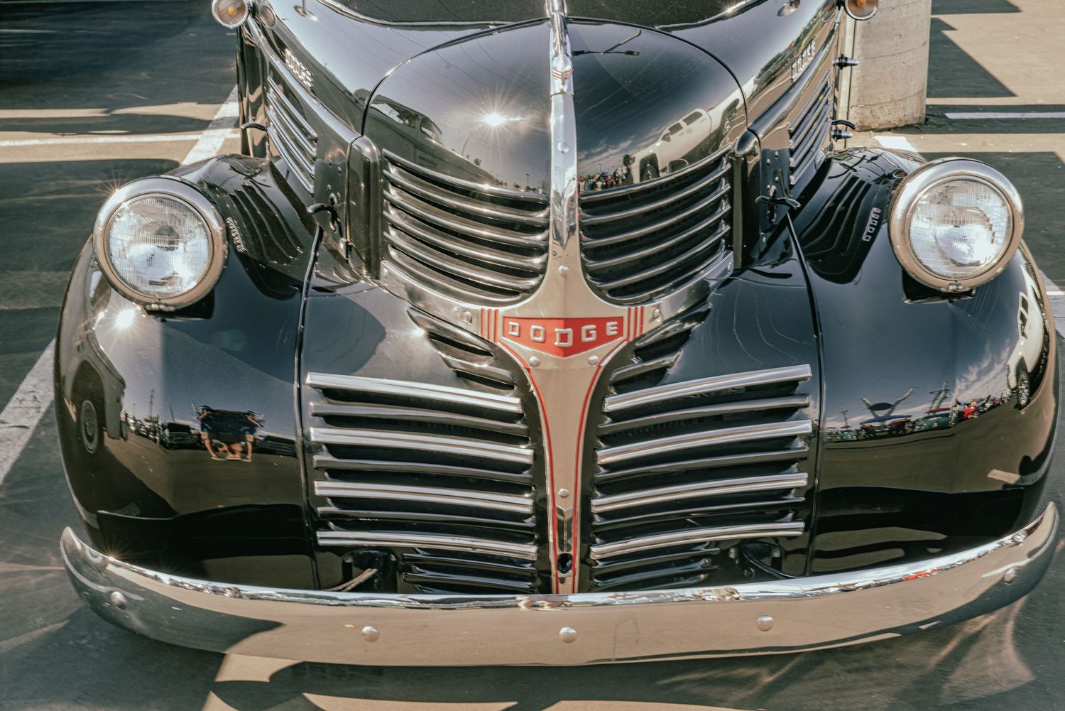Vintage black Dodge classic car front view showing chrome grille, dual headlights, and iconic hood ornament on pavement.