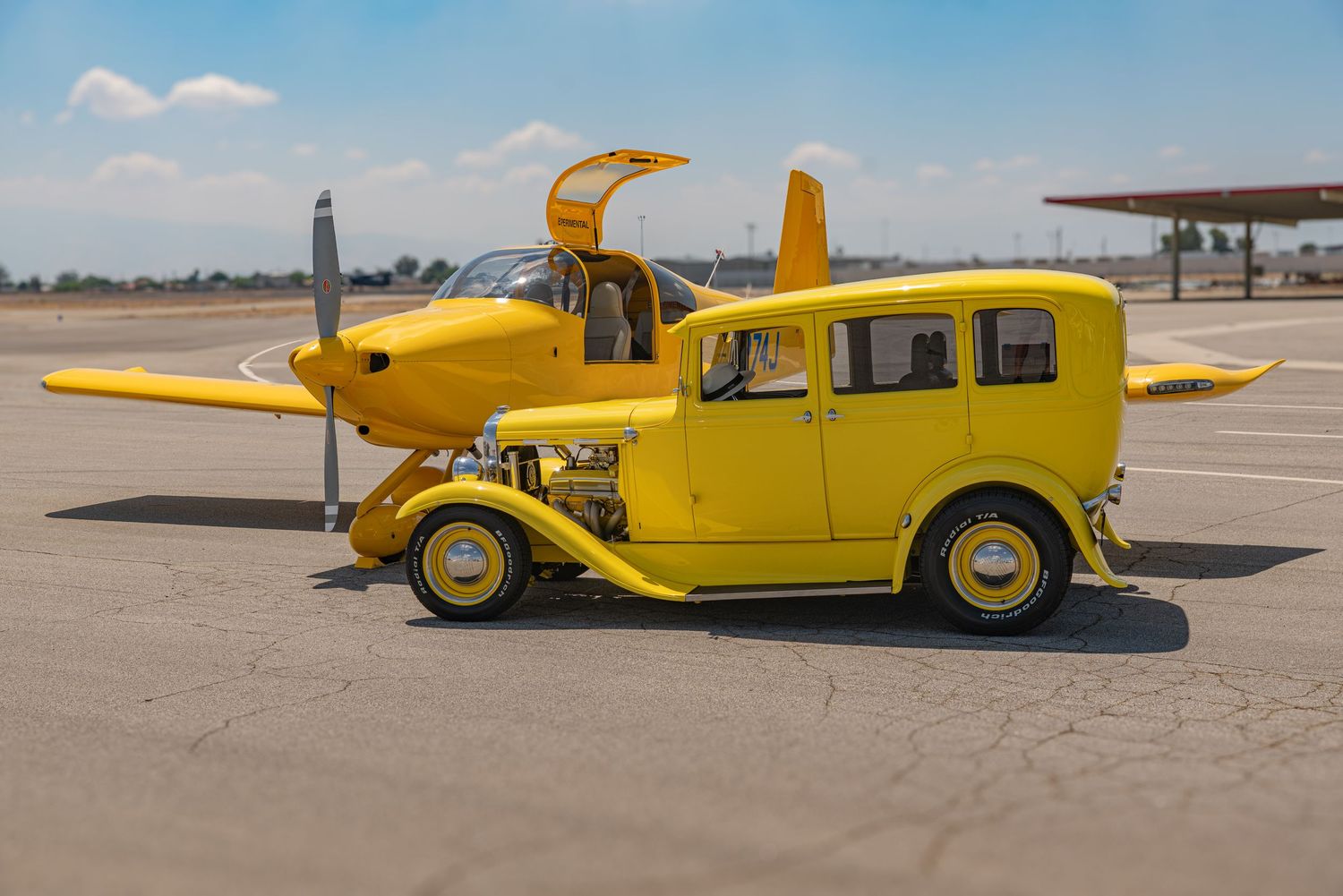 Yellow vintage car-plane hybrid vehicle parked on tarmac with propeller and wings attached, showcasing a unique automotive-aviation fusion.