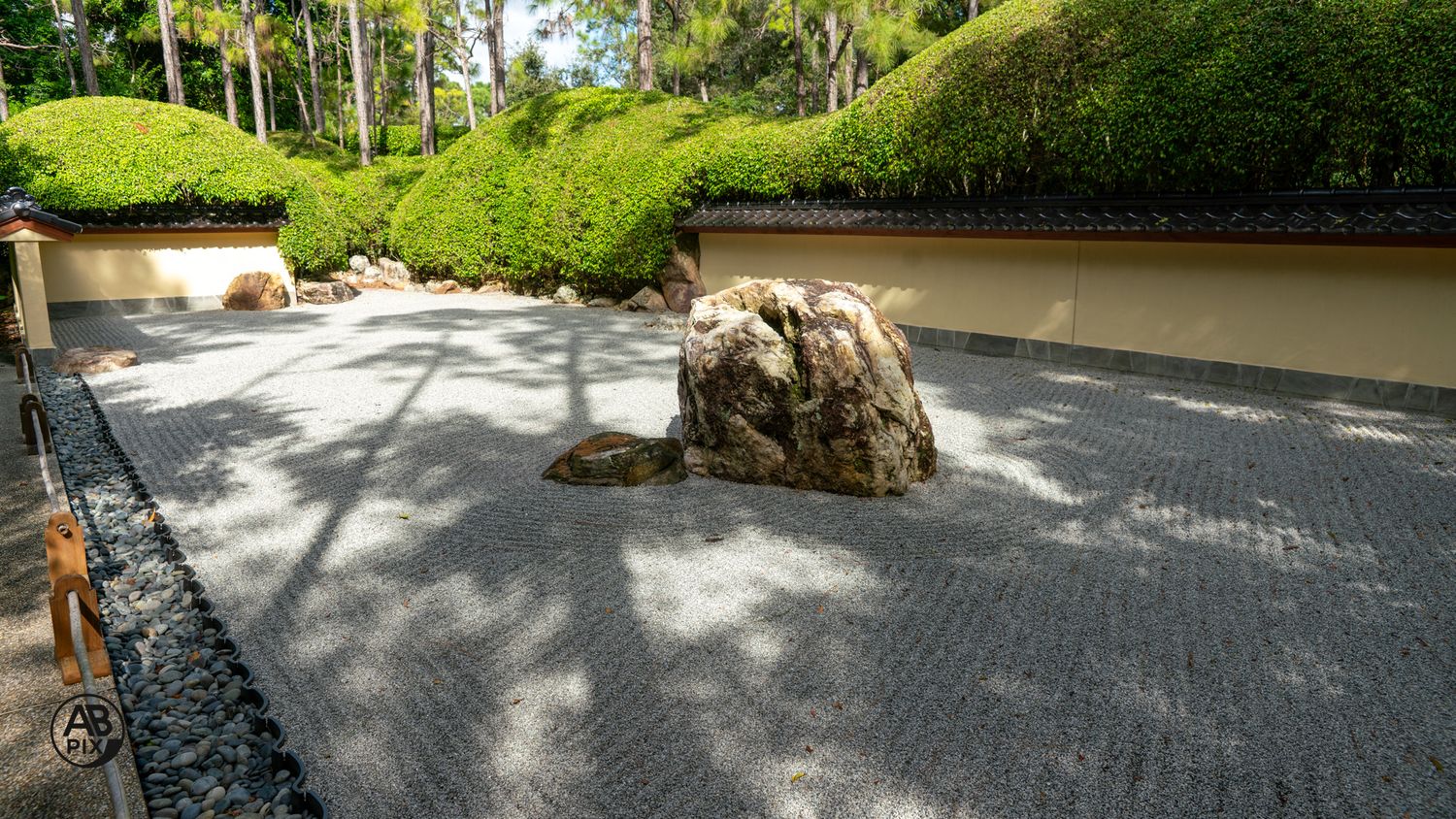 Japanese zen garden featuring a large natural rock centerpiece in raked gravel with manicured hedges backdrop.