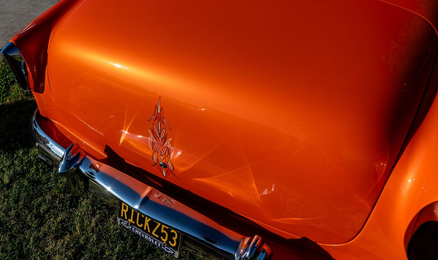 Rear view of orange classic car with flame decal and vintage license plate on green grass.