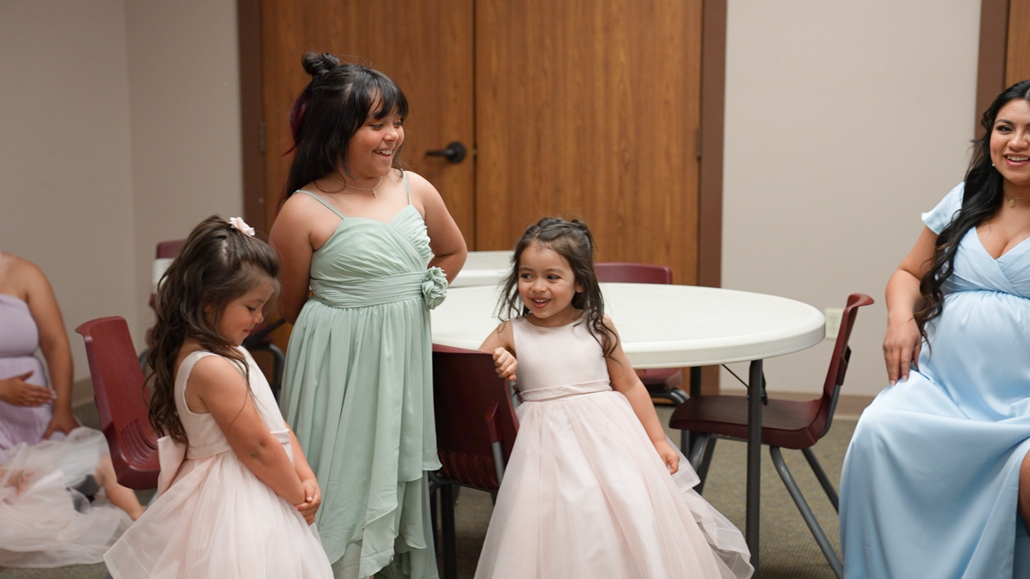 Bridesmaids in mint and blue dresses interact with flower girls in pink at a wedding reception.