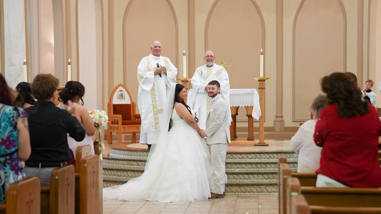 Bride and groom holding hands at church altar during wedding ceremony with priest officiating.