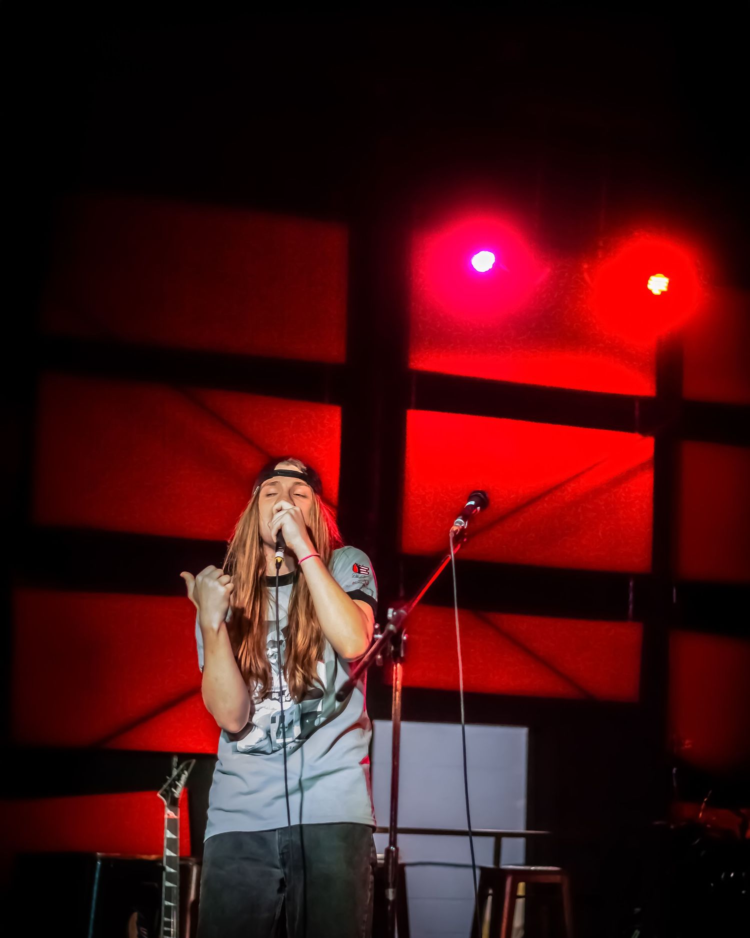 Female singer performing passionately on stage under dramatic red and pink stage lighting at night.