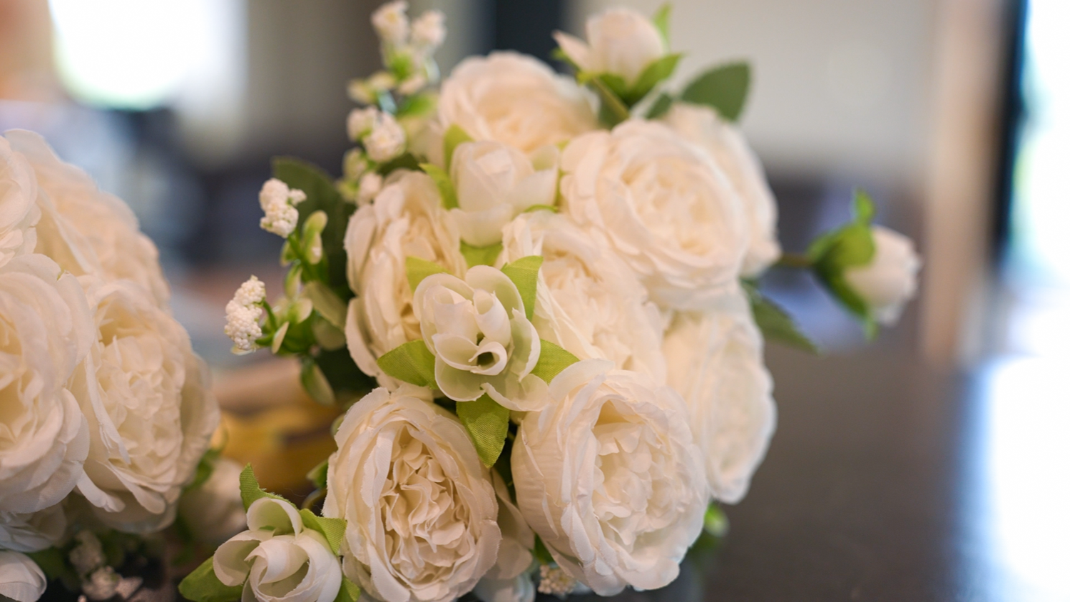 Close-up of elegant white rose wedding bouquet with green accents and small white blooms.