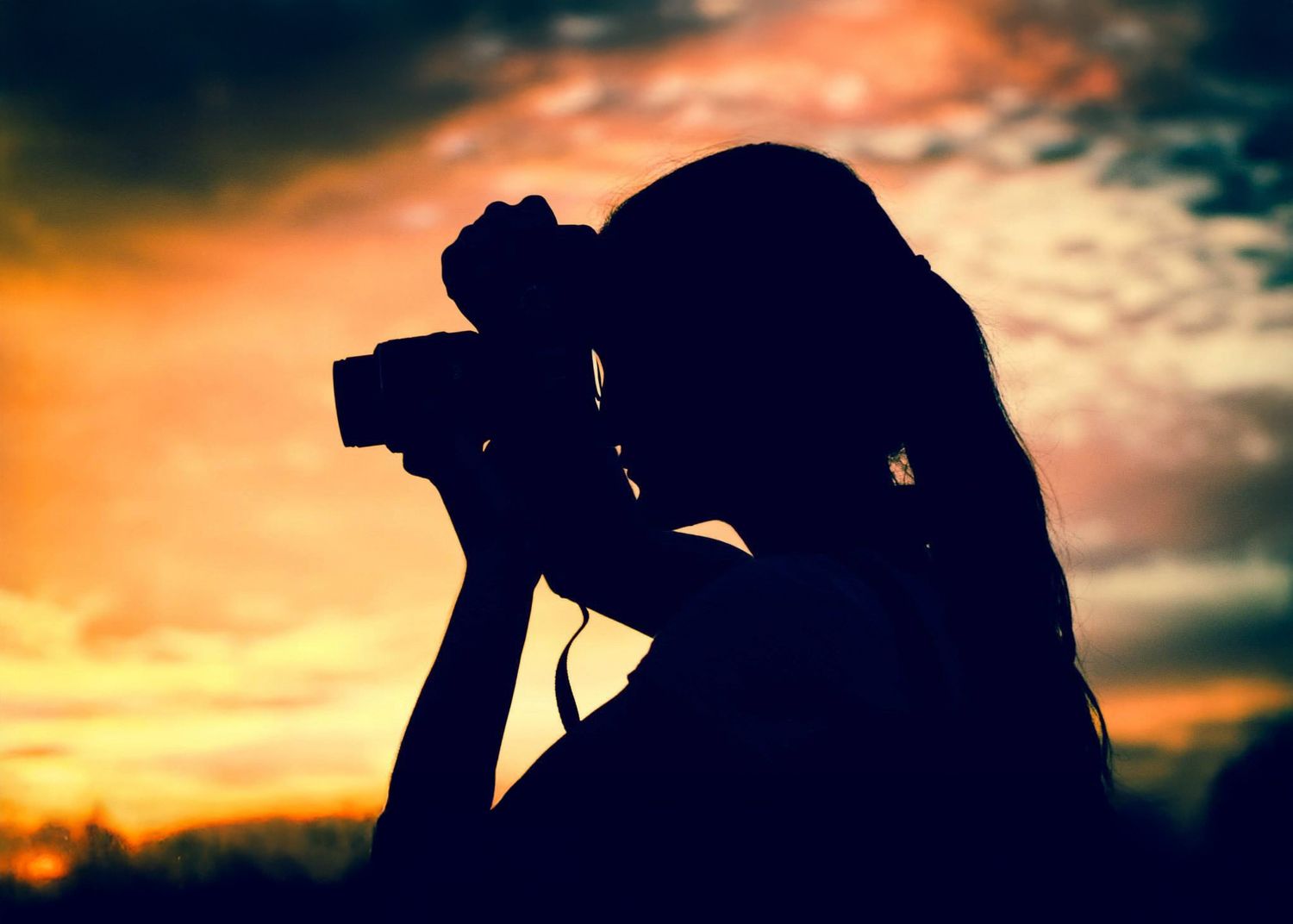 Silhouette of a woman photographing with a camera against a dramatic colorful sunset sky.