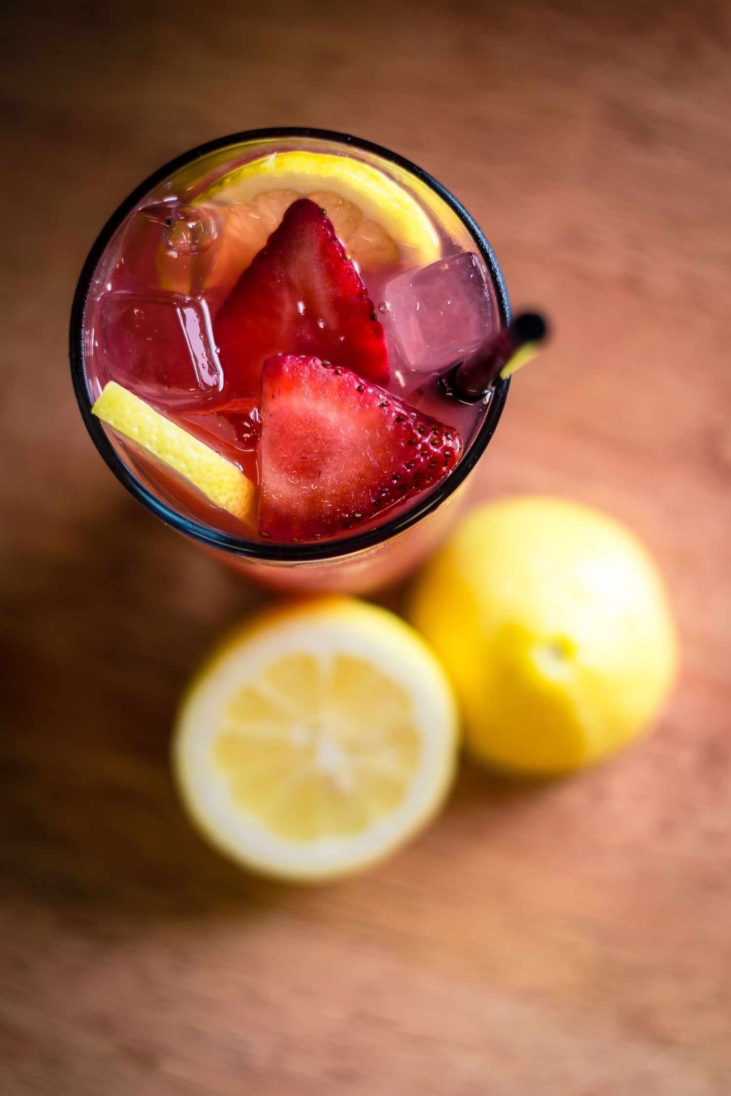 Top view of a refreshing strawberry lemonade cocktail with ice cubes and fresh lemons on a wooden surface.