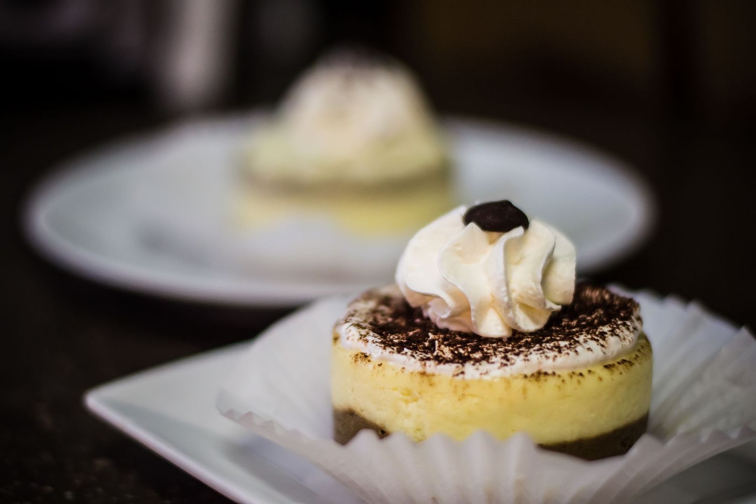 Two elegant mini cheesecakes topped with whipped cream and chocolate shavings served on white plates.