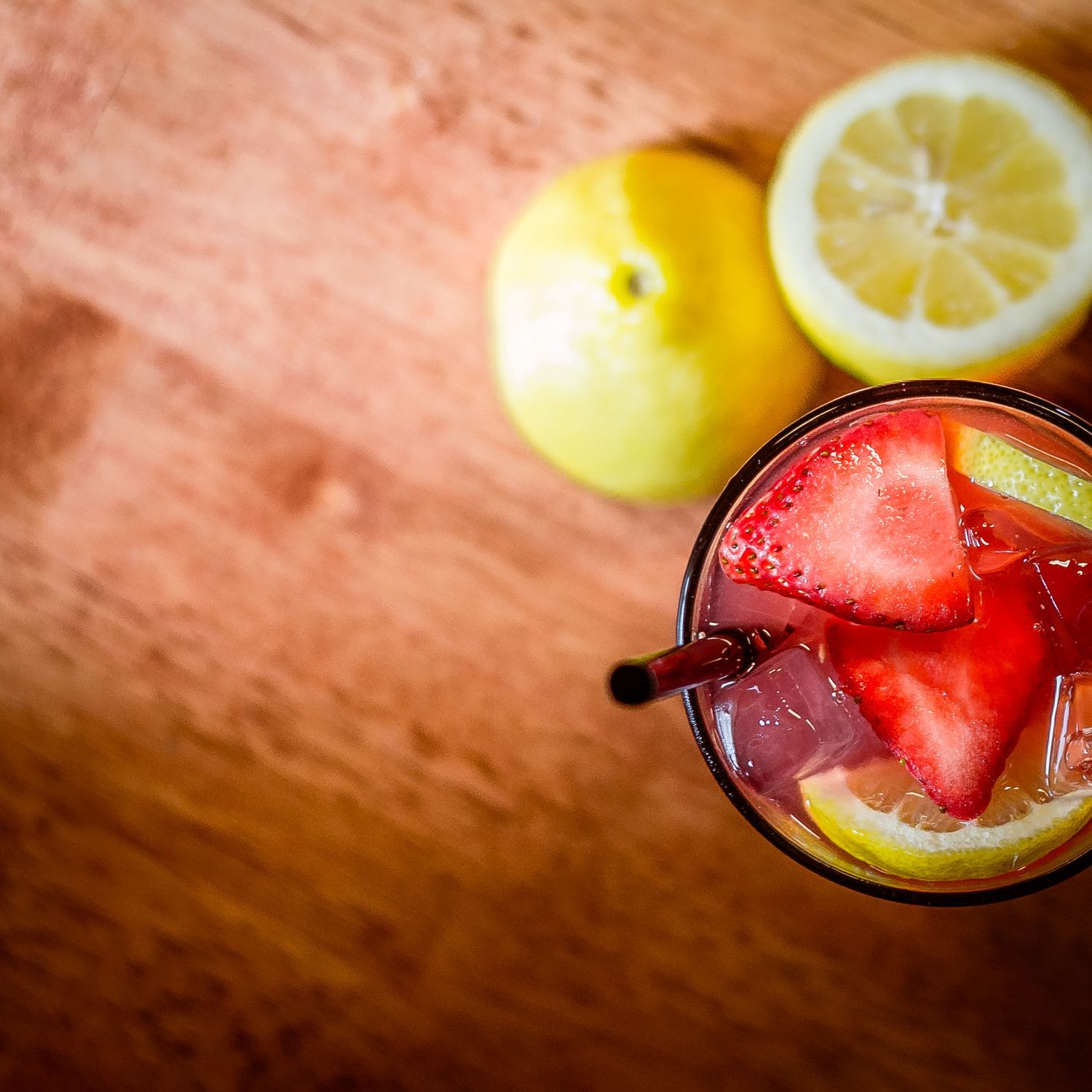 A refreshing strawberry lemonade cocktail with ice in a glass, garnished with fresh strawberries and lemon slices on a wooden surface.