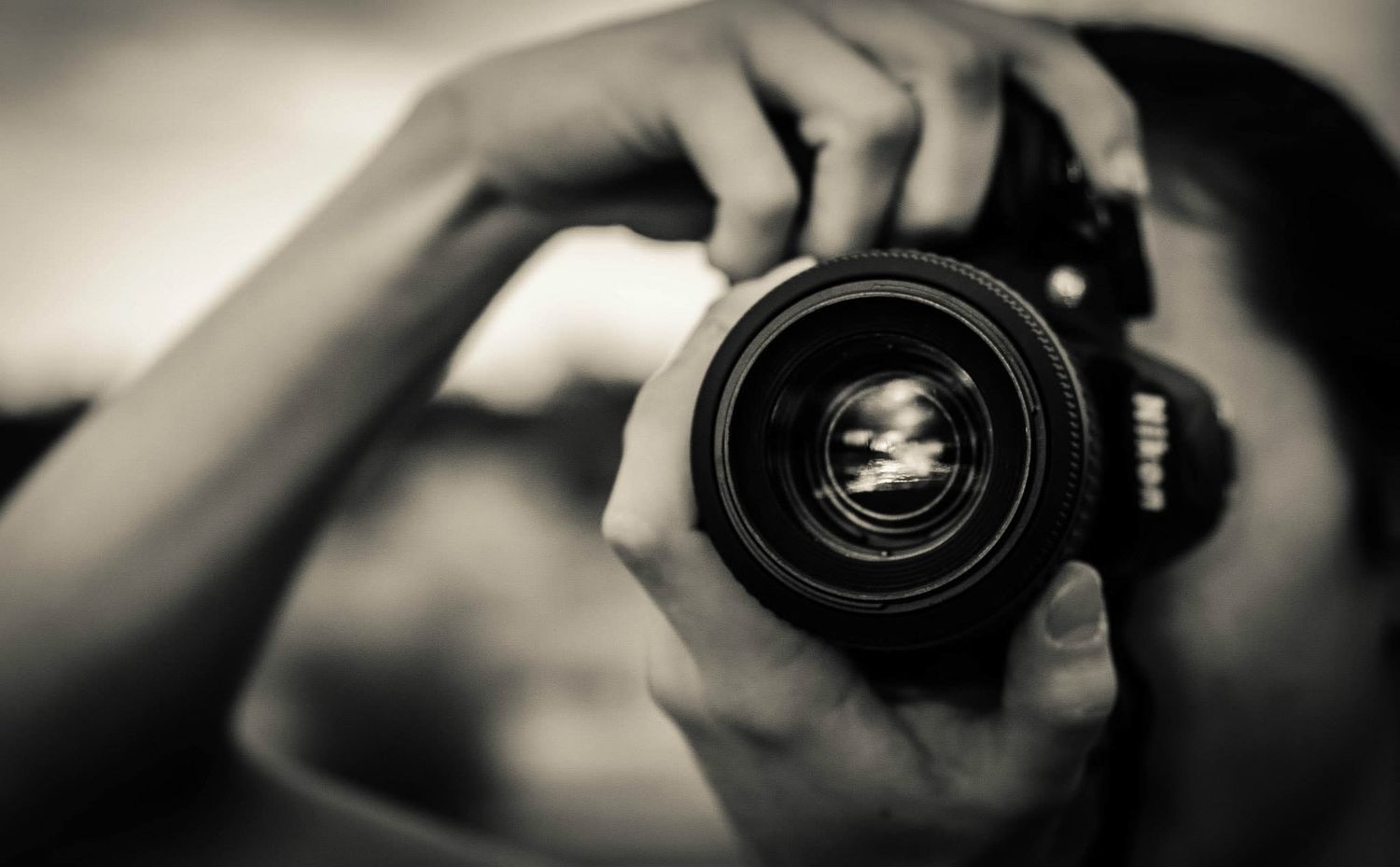 Close-up black and white photo of hands holding a Nikon DSLR camera.