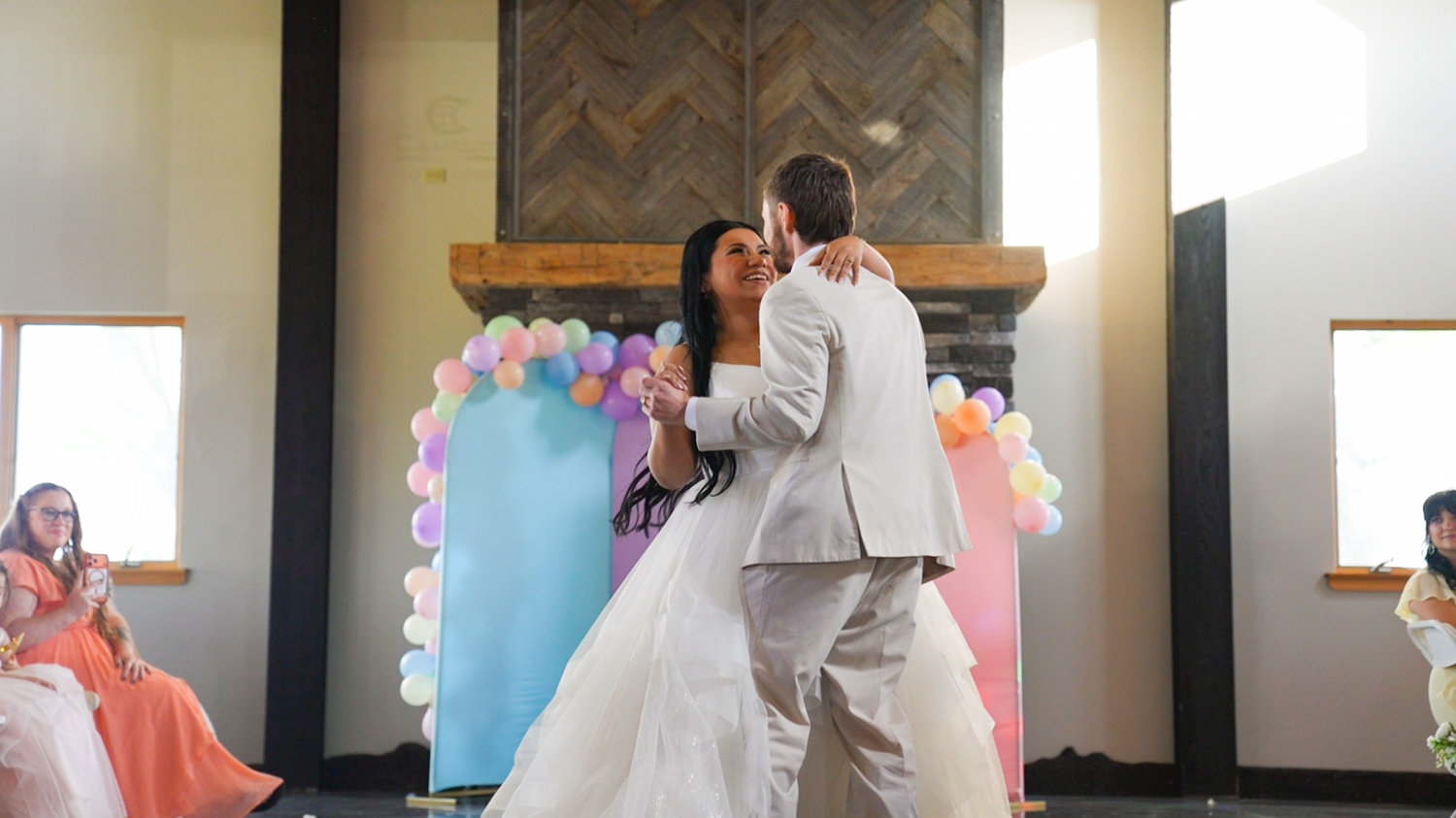 Bride and groom sharing first dance in front of colorful balloon arch at wedding reception.