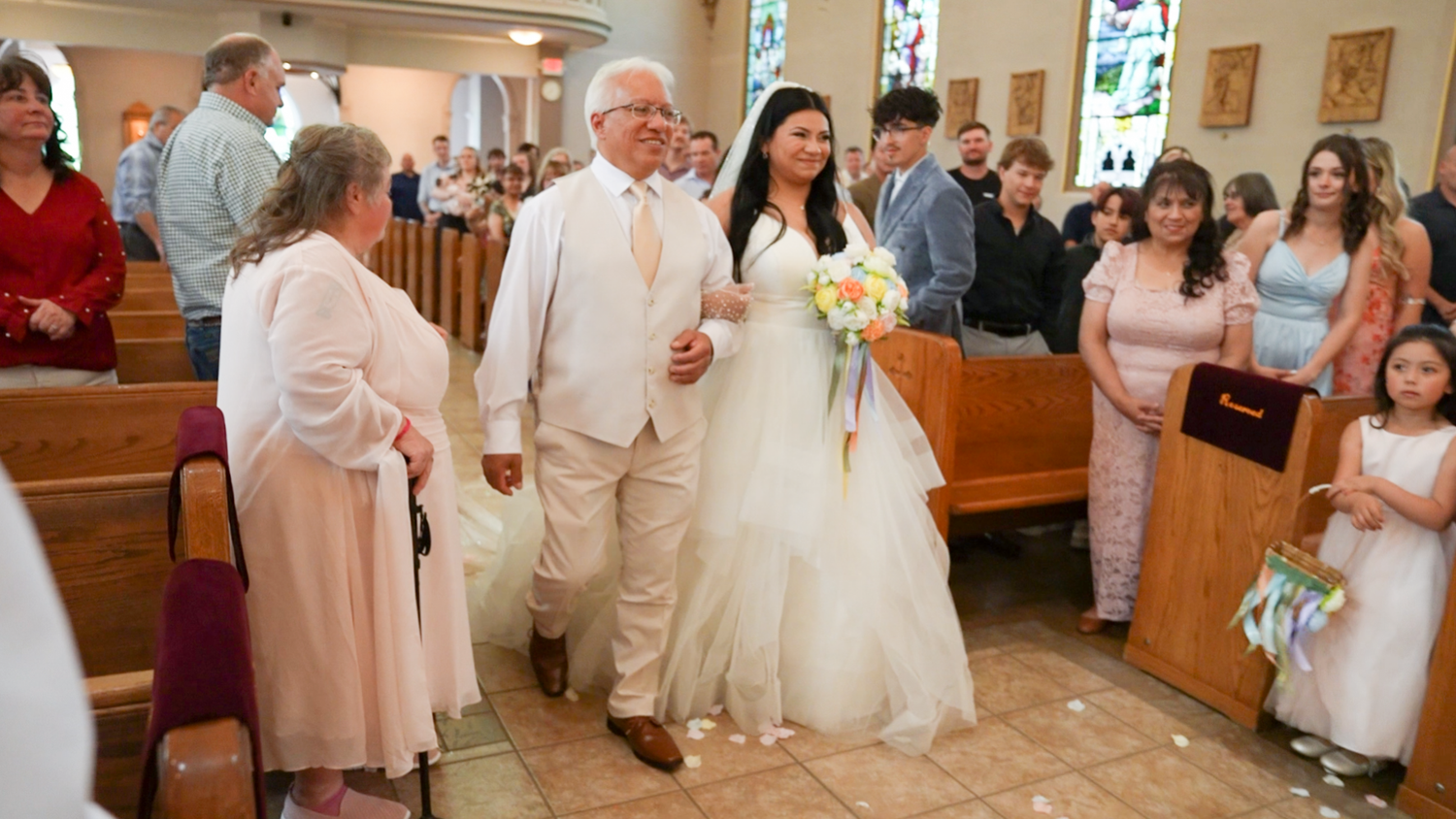 Bride walks down church aisle escorted by father during traditional wedding ceremony.