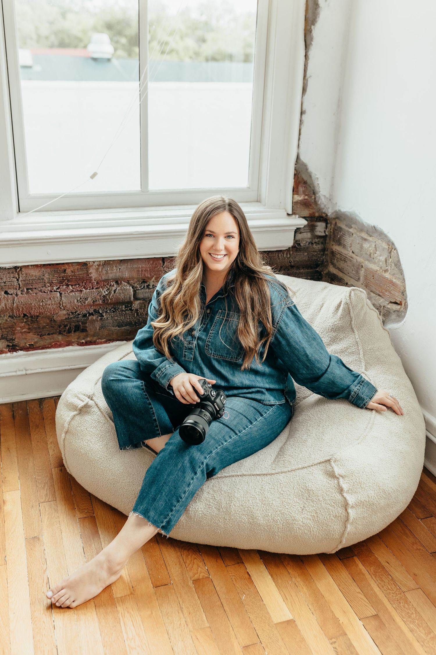 Four lifestyle photos of someone lounging on a beige bean bag chair while wearing denim against white walls and wood floors.